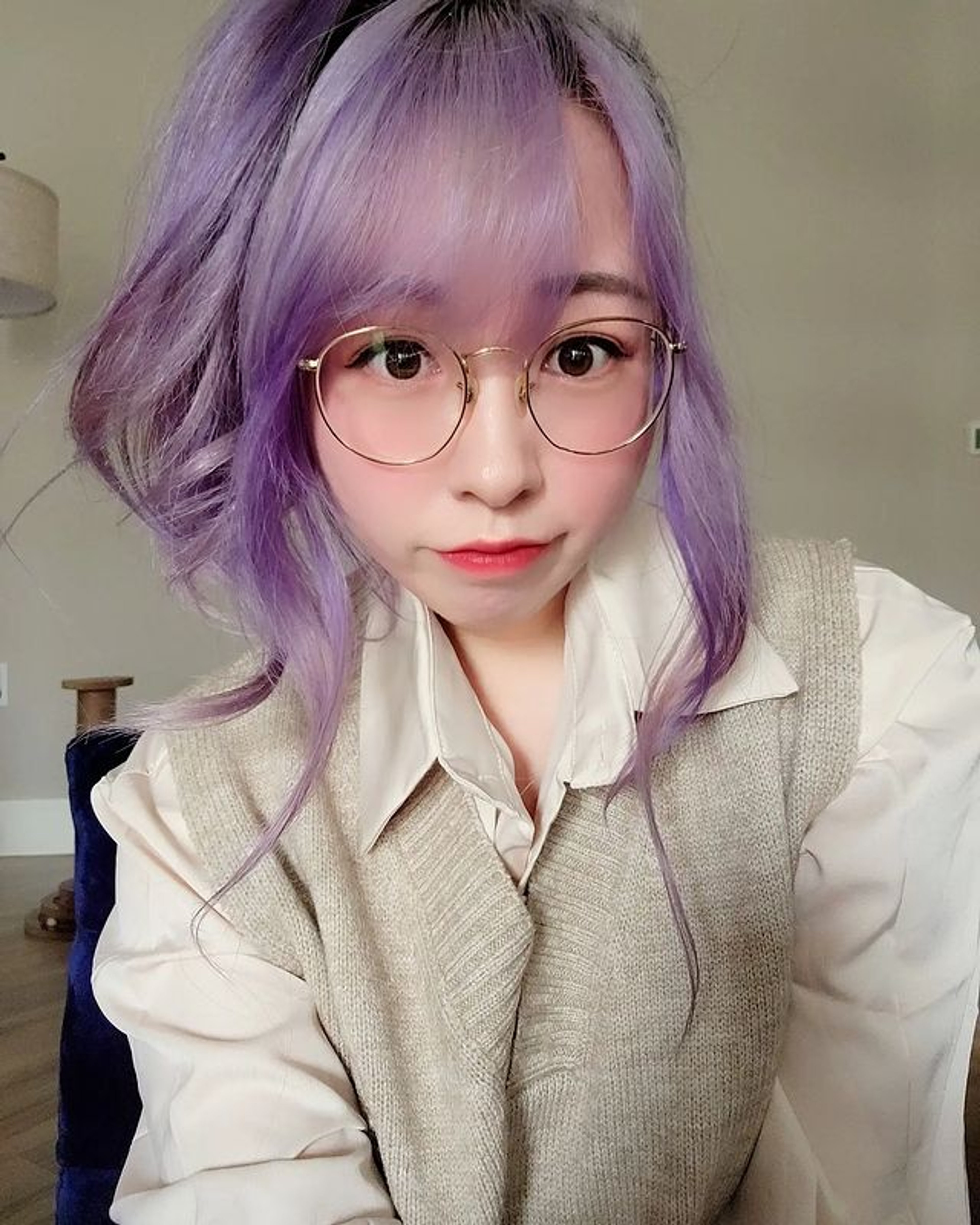A young woman with purple hair and glasses smiling at the camera