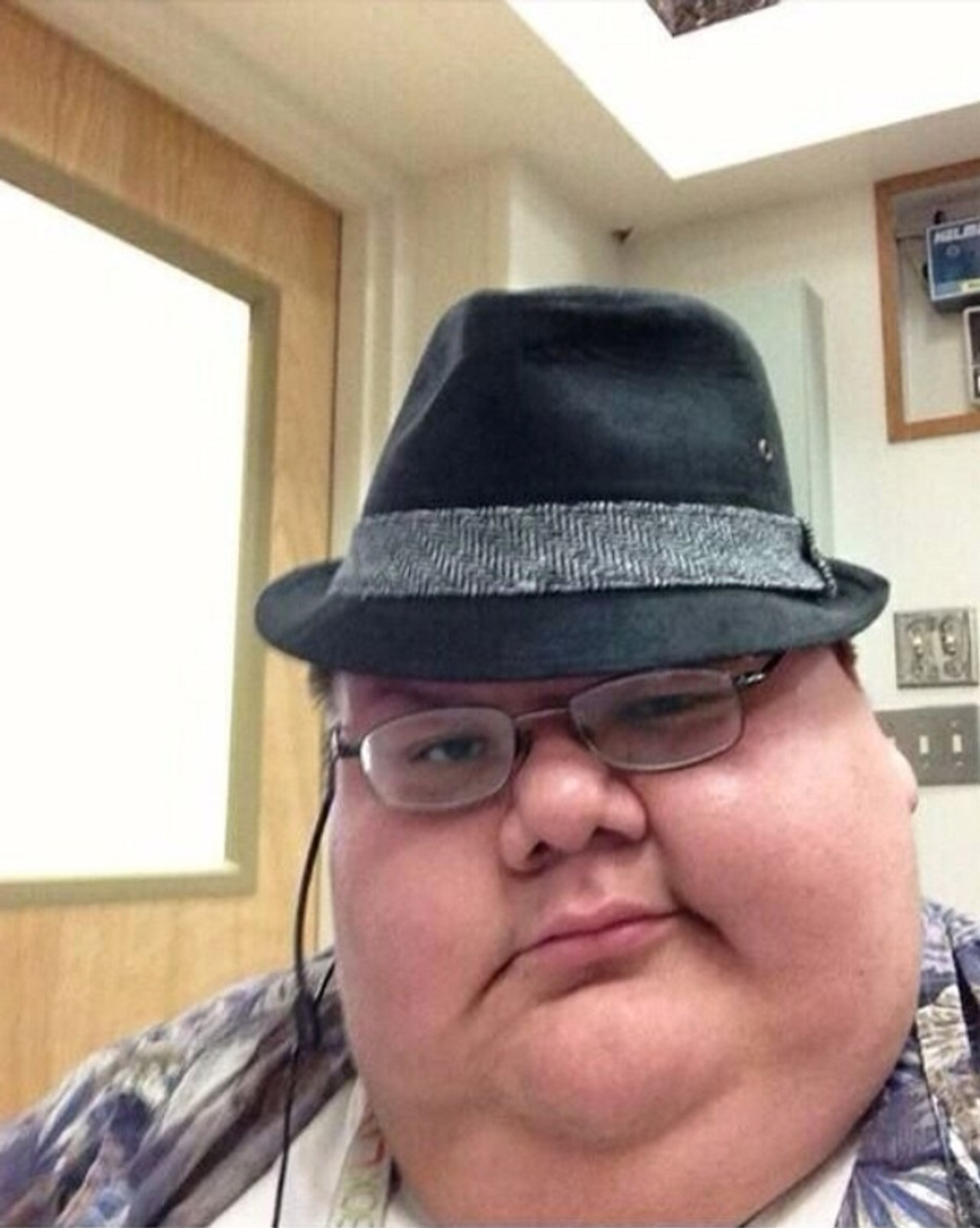 An obese man wearing glasses and a fedora