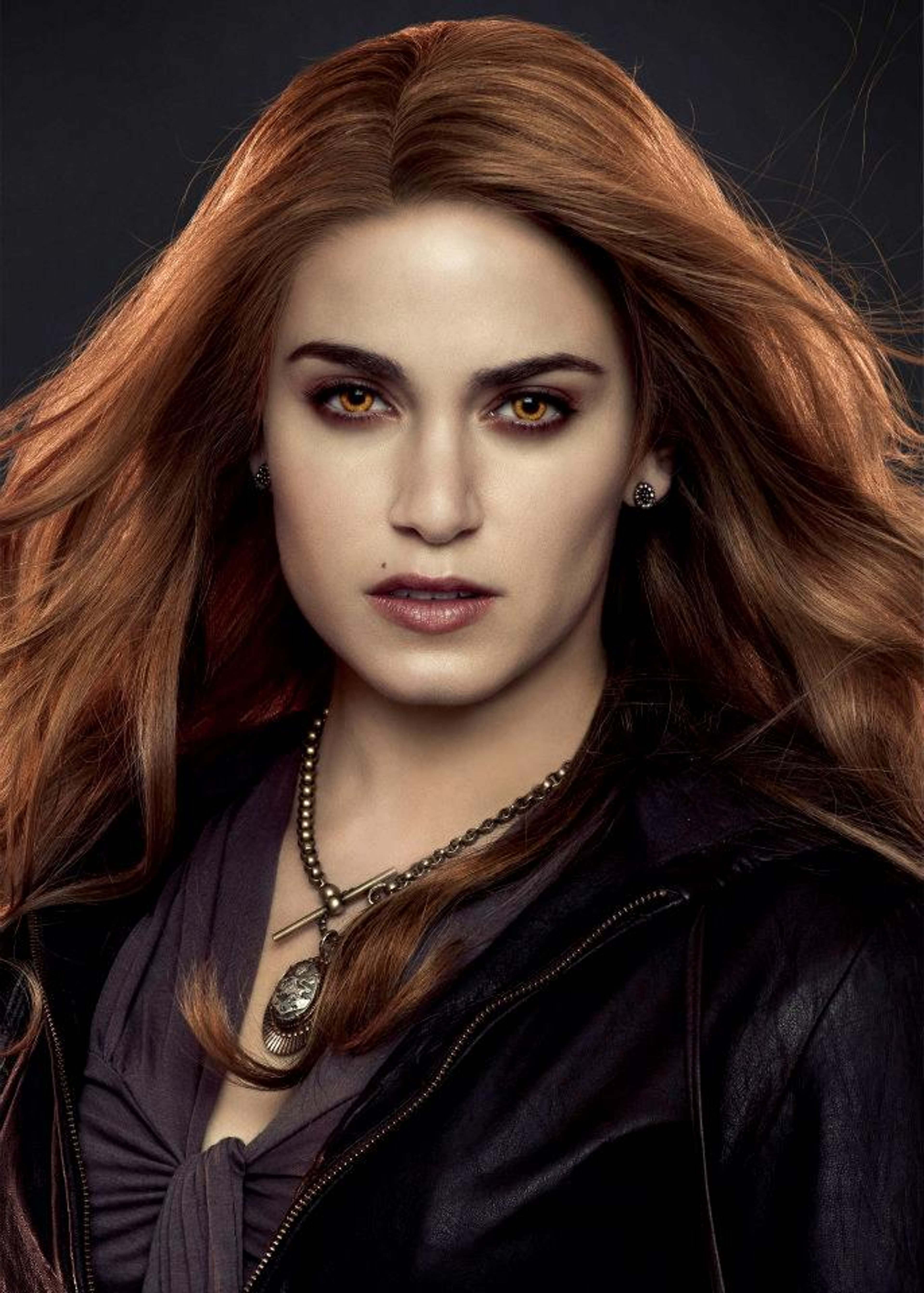 A beautiful, red-haired woman with intense blue eyes and a mysterious expression, wearing a black leather jacket.