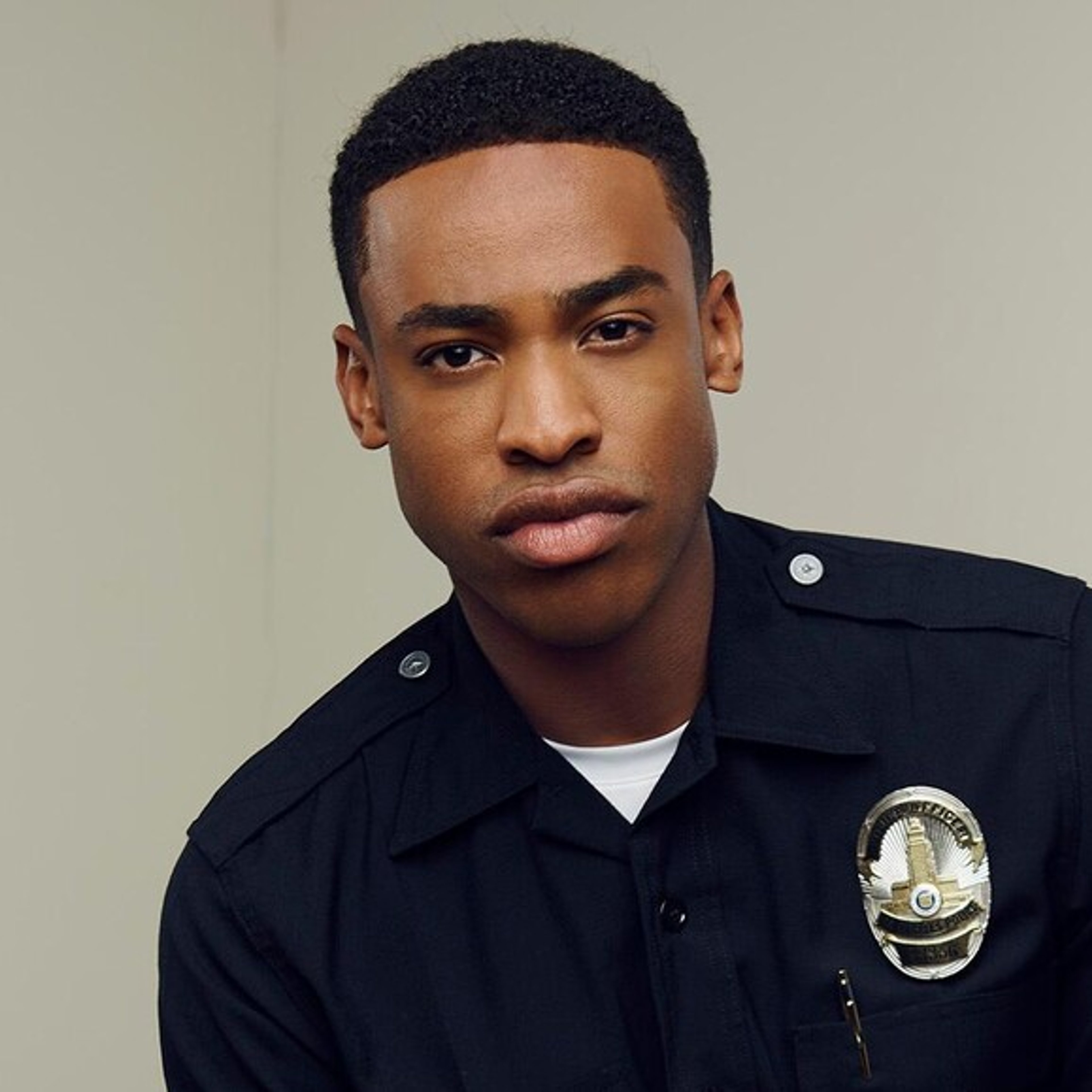 A young Black police officer in a dark blue uniform with a serious expression