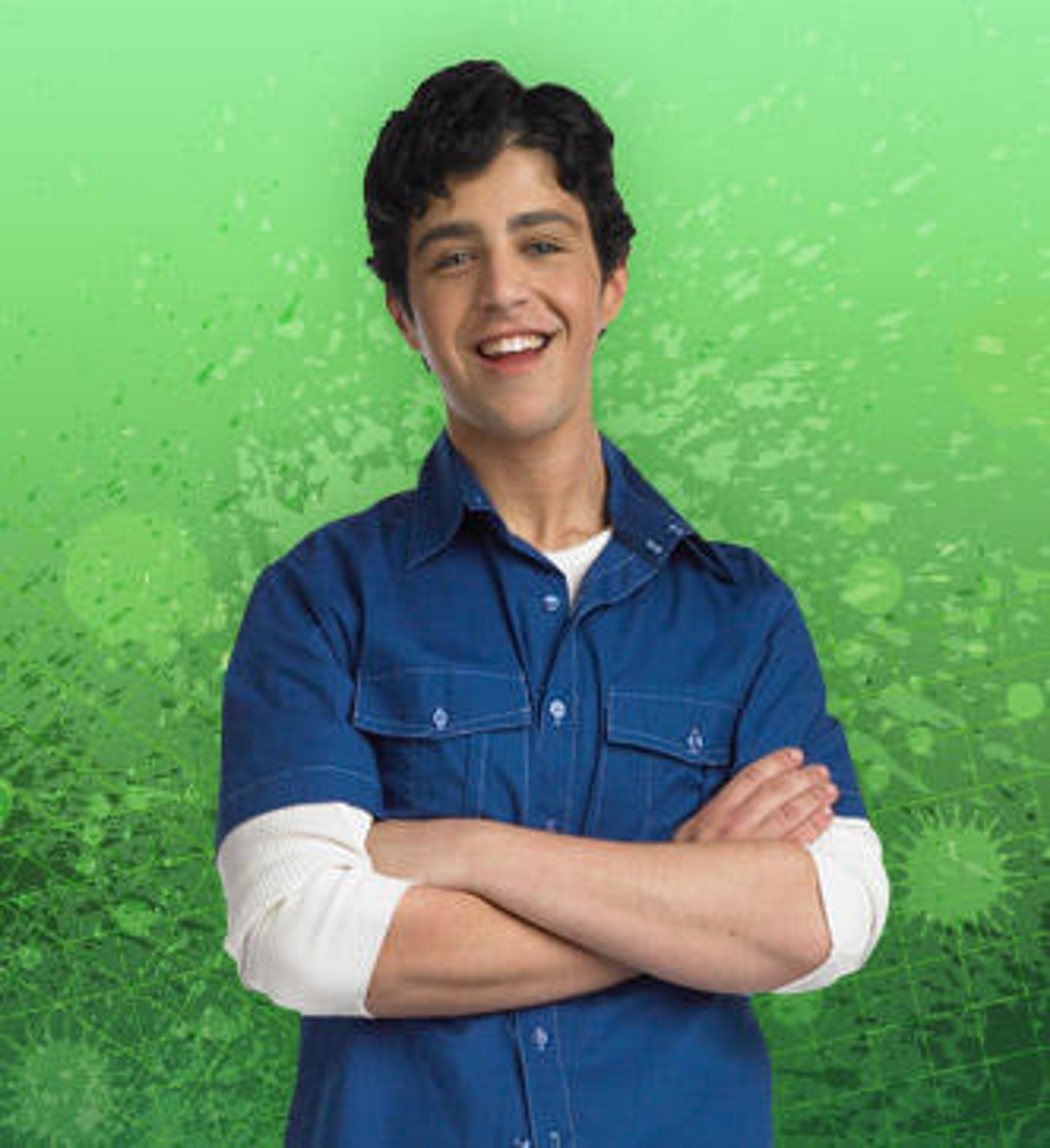 A smiling young man with dark hair wearing a blue denim shirt against a green background.