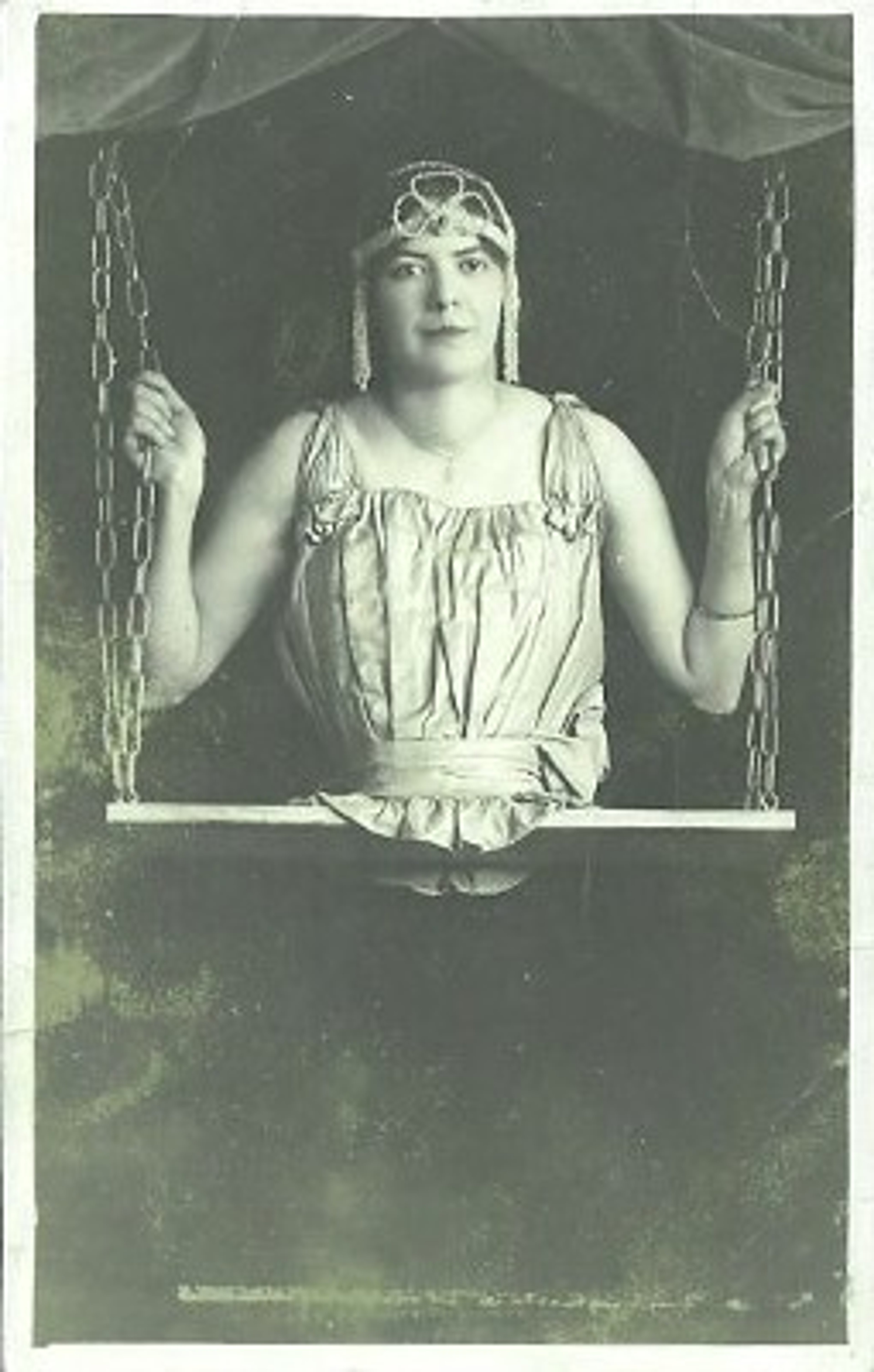 A woman in a long dress and headpiece sitting on a swing