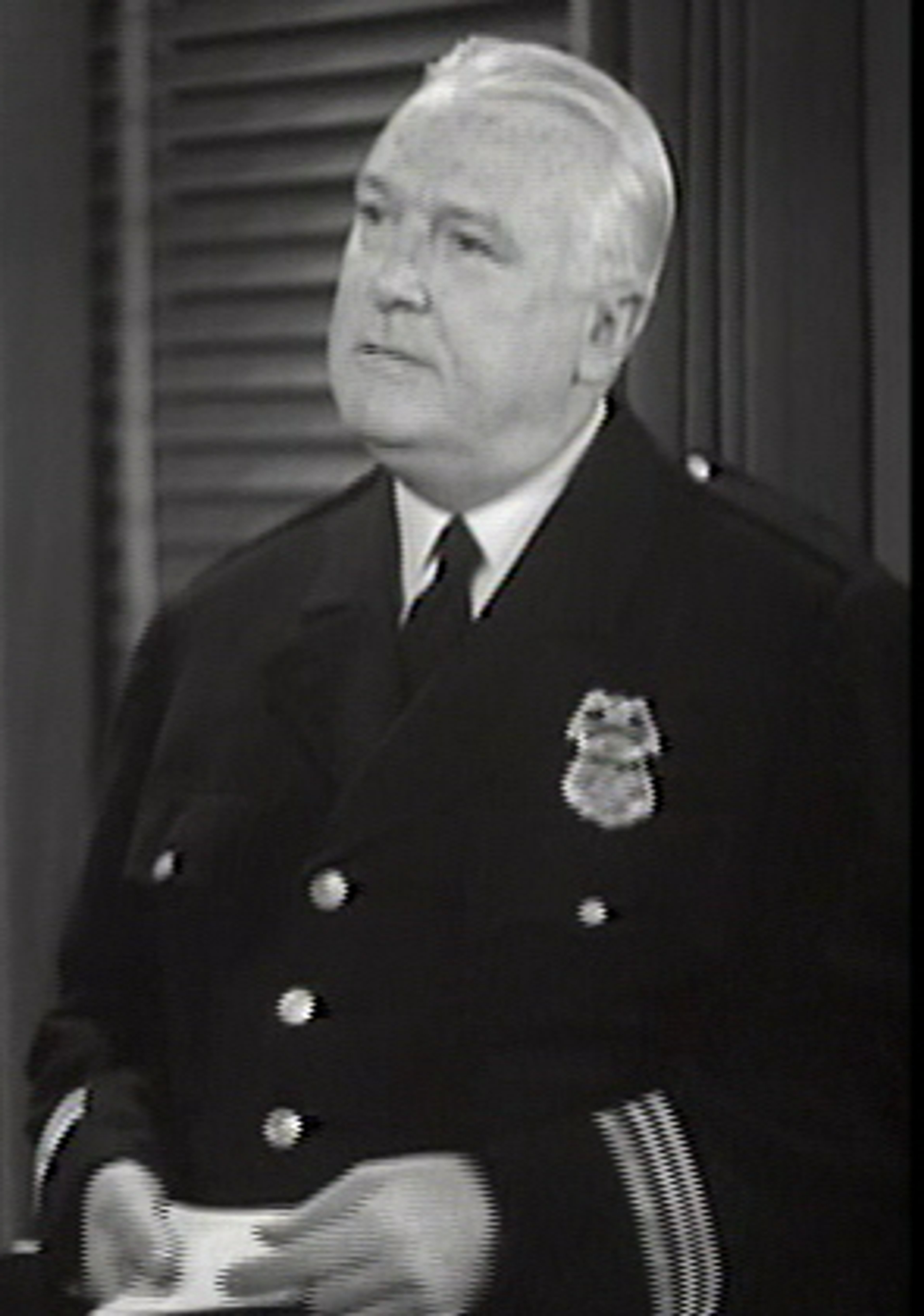 An older man in a police uniform, likely a police captain or high-ranking officer.