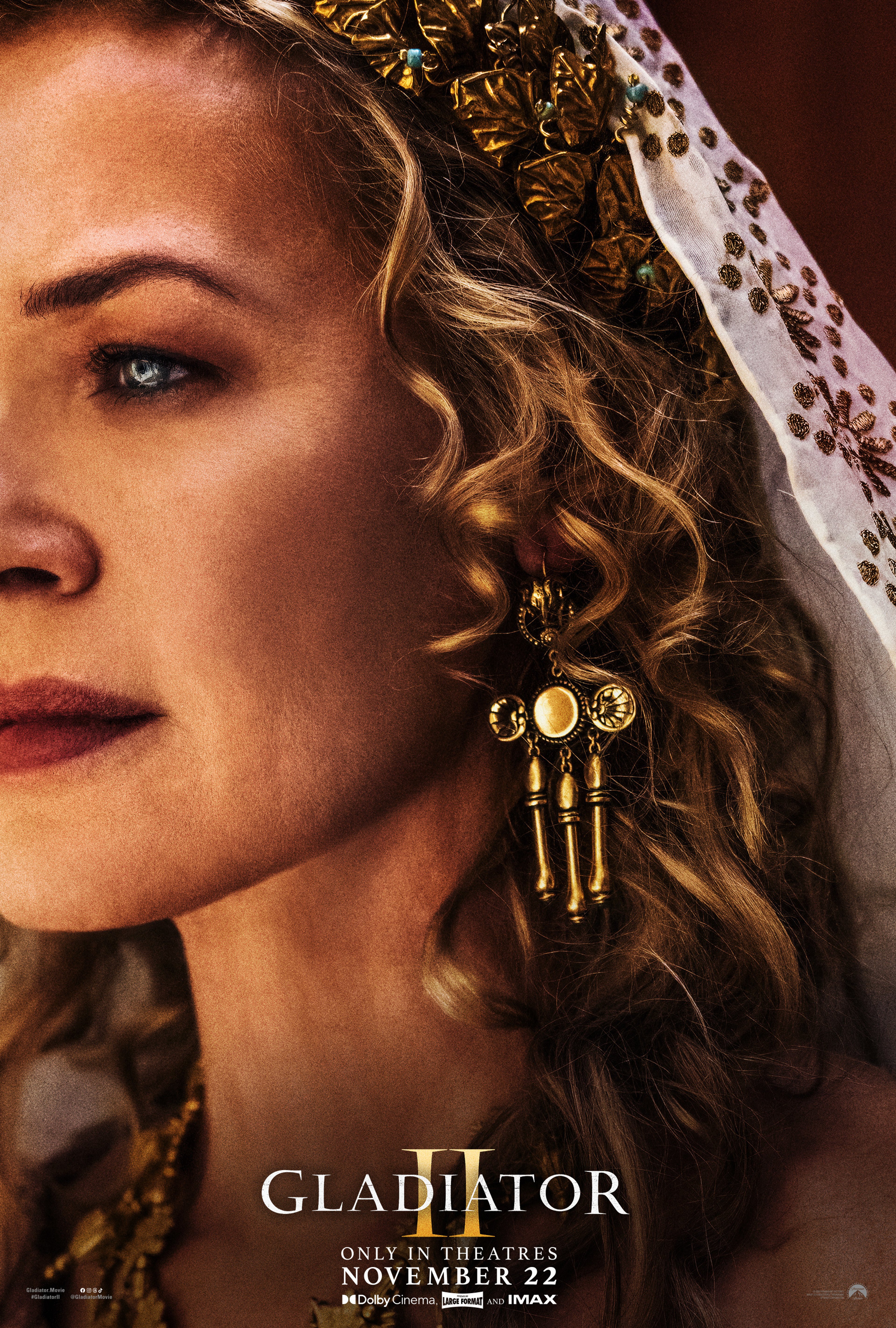 A woman with curly blonde hair wearing a gold headdress and jewelry, with a serious expression on her face.