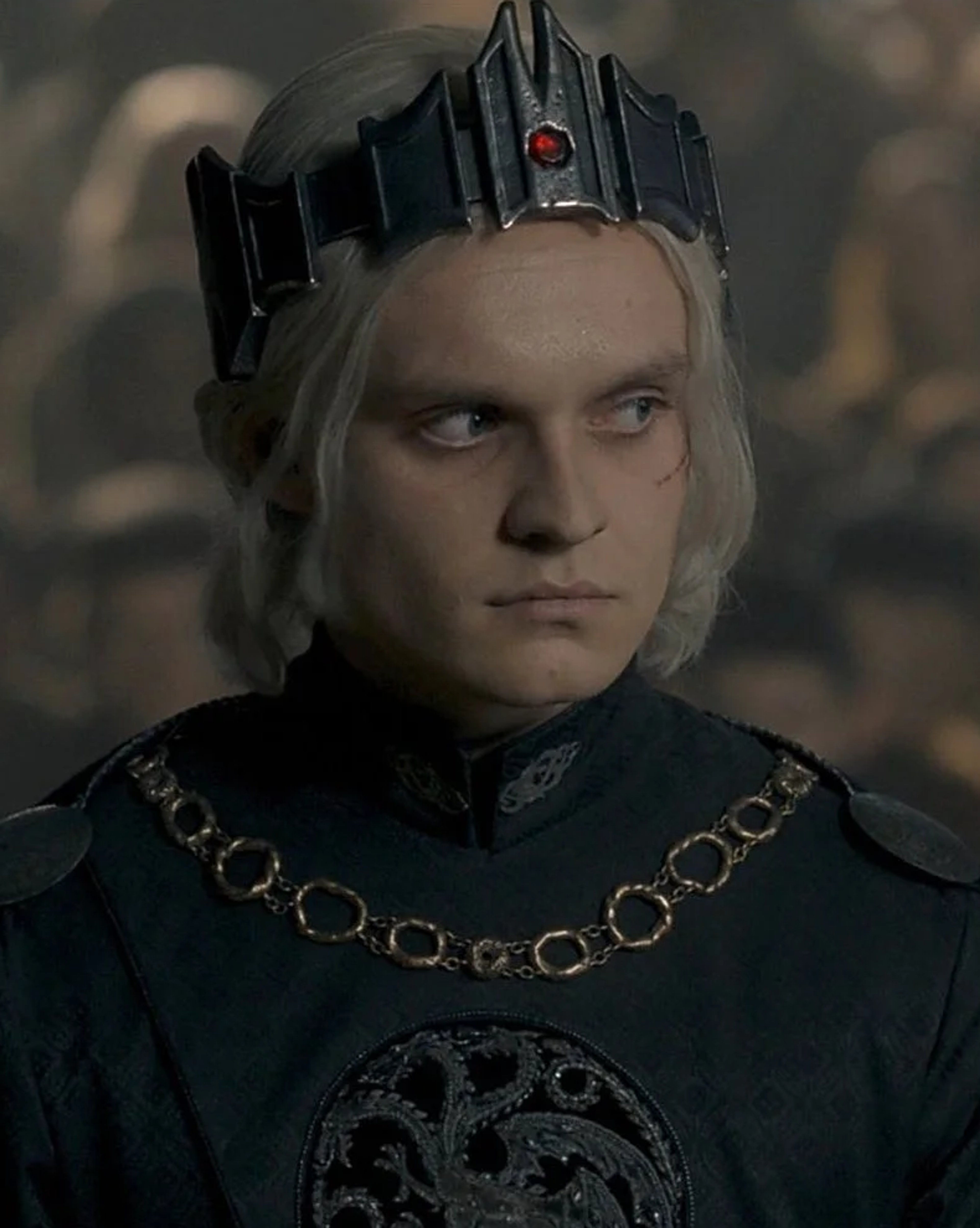 A man with pale skin, long white hair, and a stern expression wearing a dark outfit with a crown-like headpiece