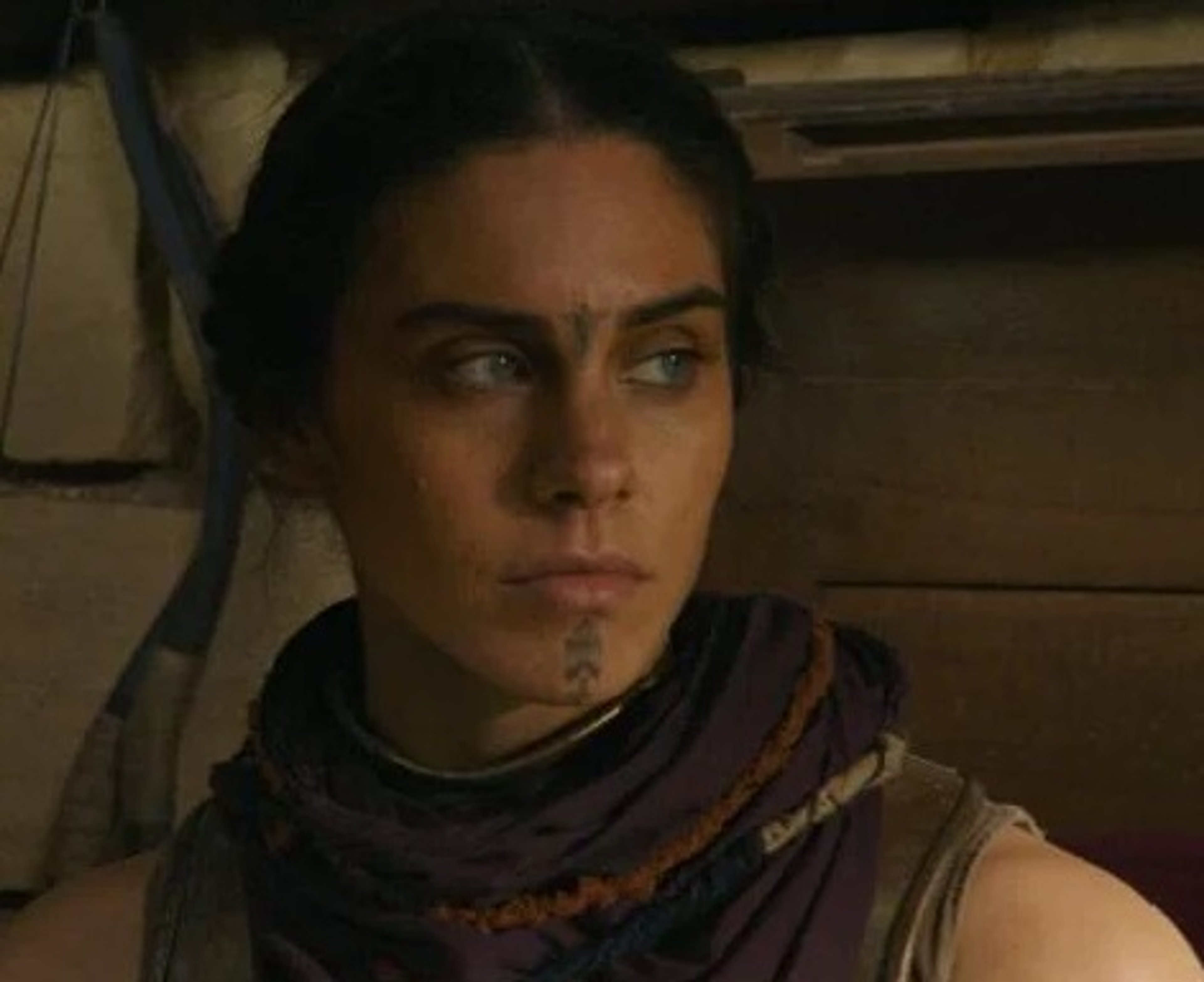 A woman with dark hair and a serious expression, wearing a scarf or shawl around her head and shoulders.