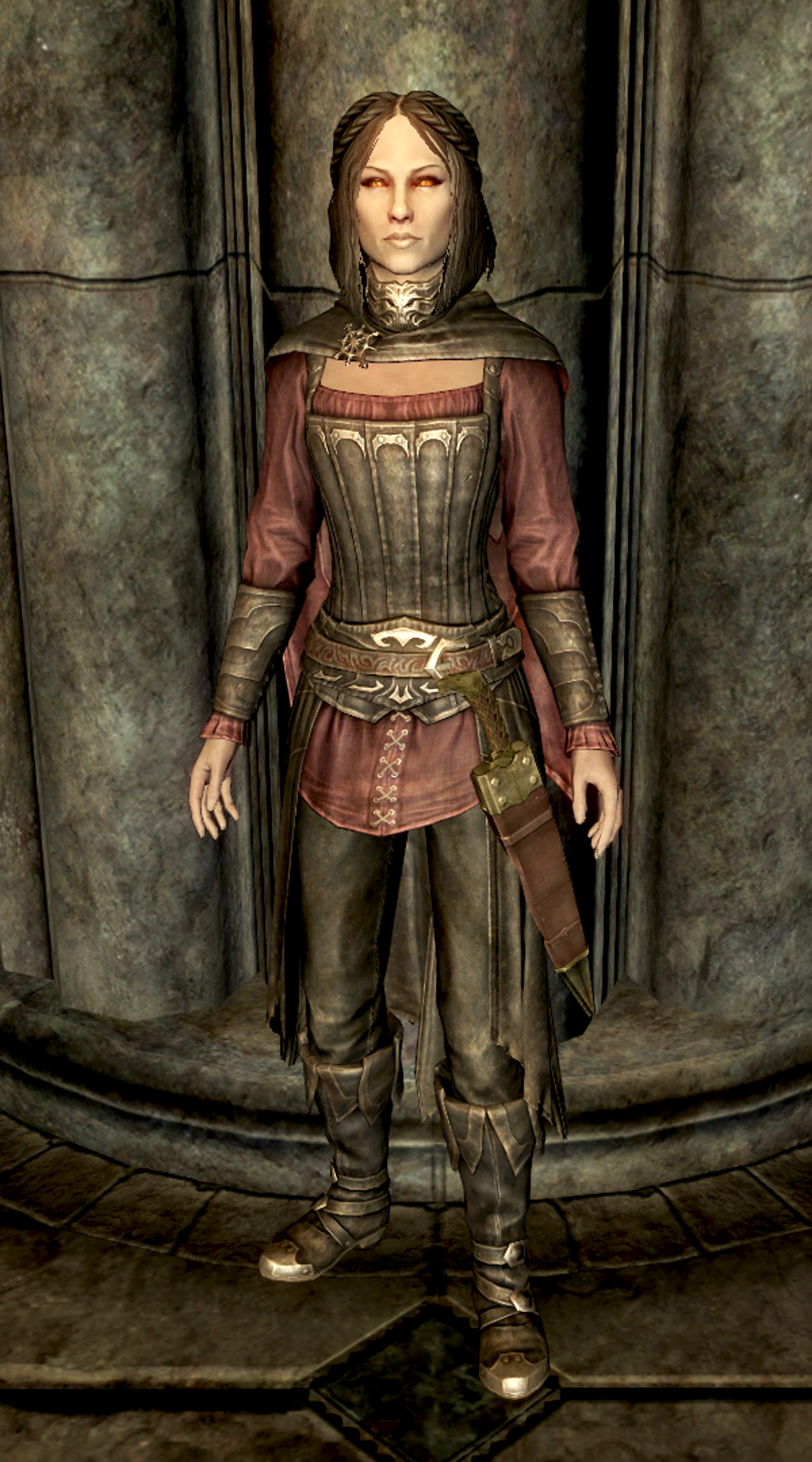 A female character in a red and gold armored outfit standing in a dimly lit, stone-walled environment.