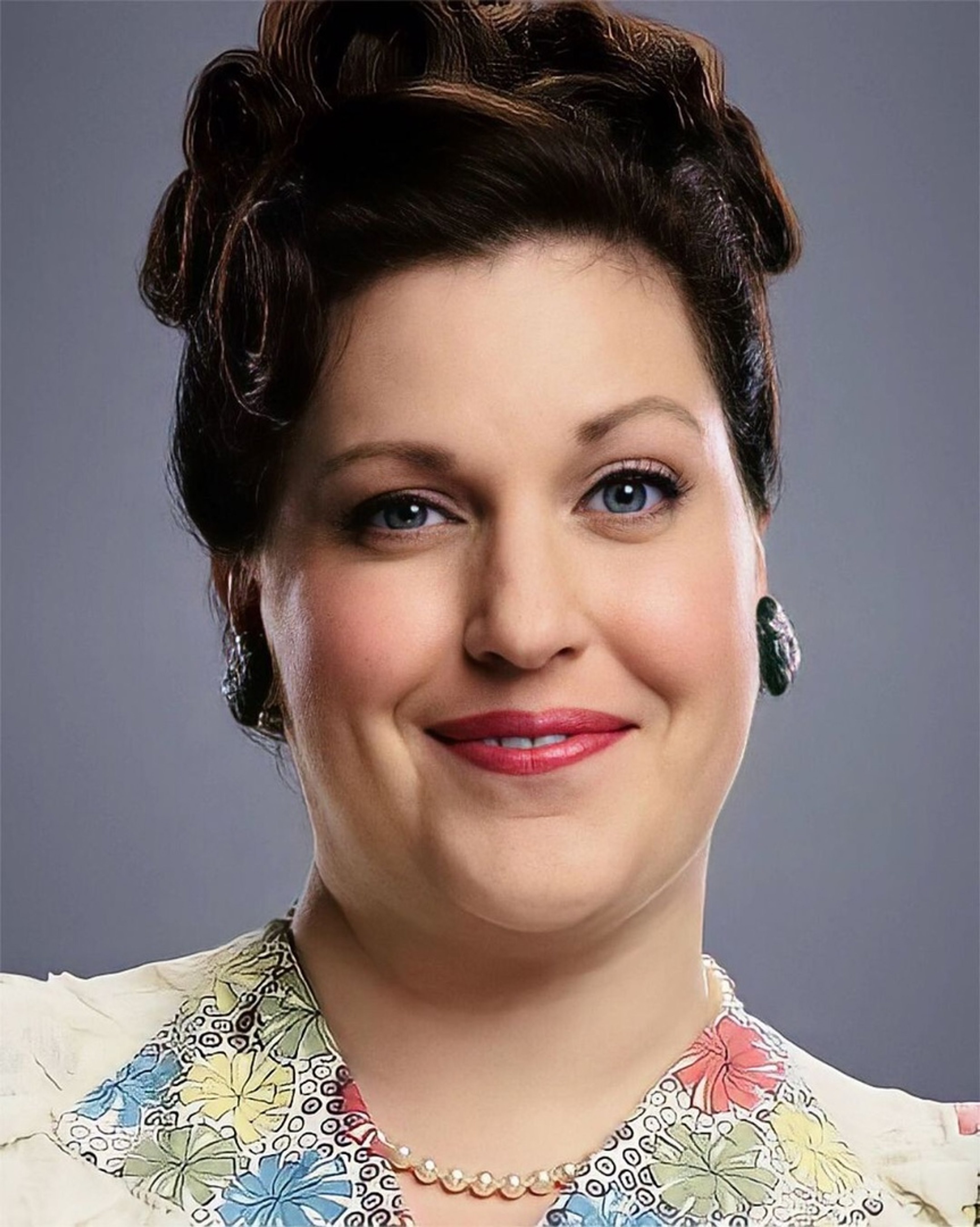 A middle-aged woman with curly brown hair and a warm, friendly expression, wearing a floral print dress.