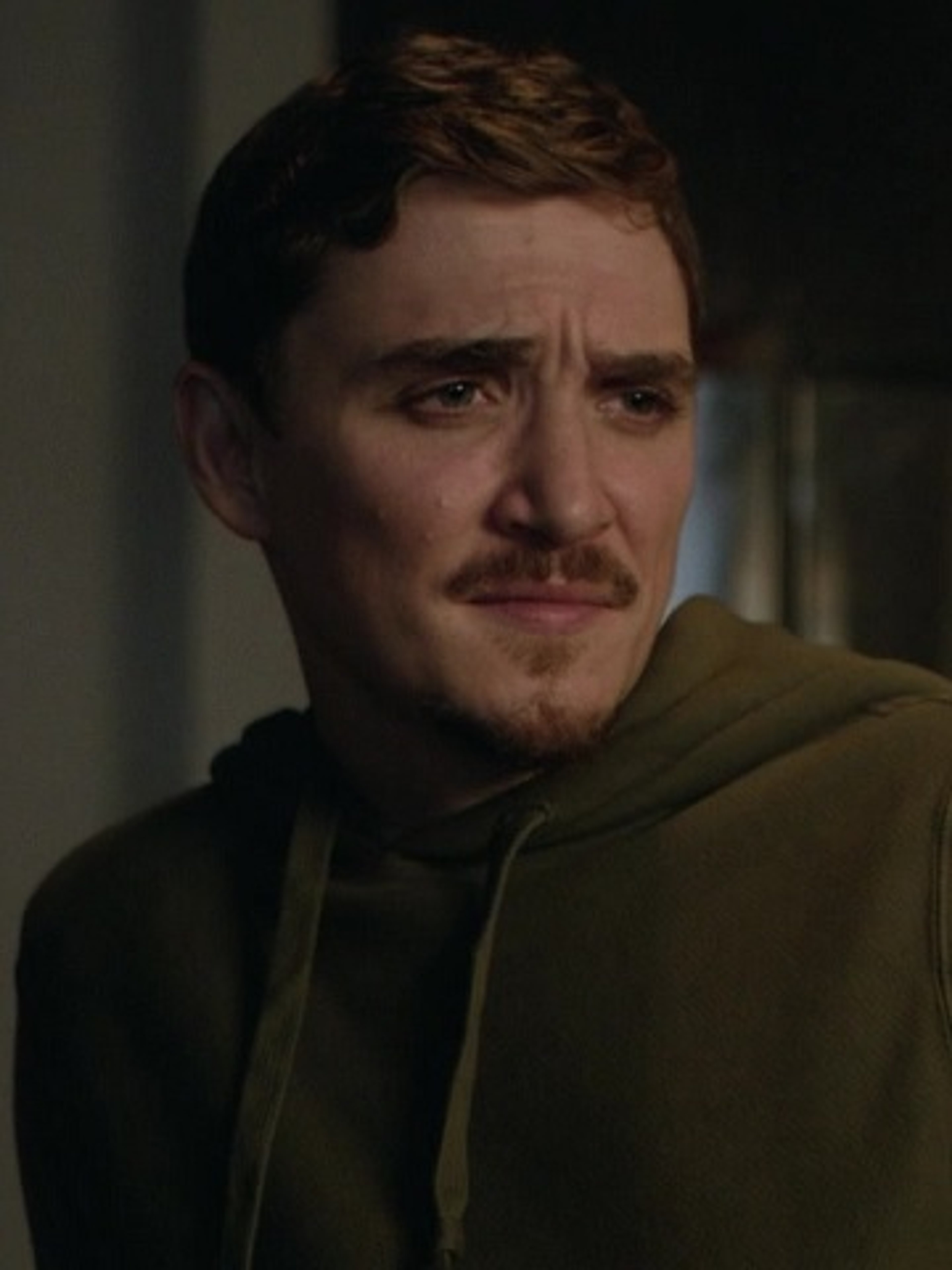 A man with a serious expression wearing a dark green hooded jacket