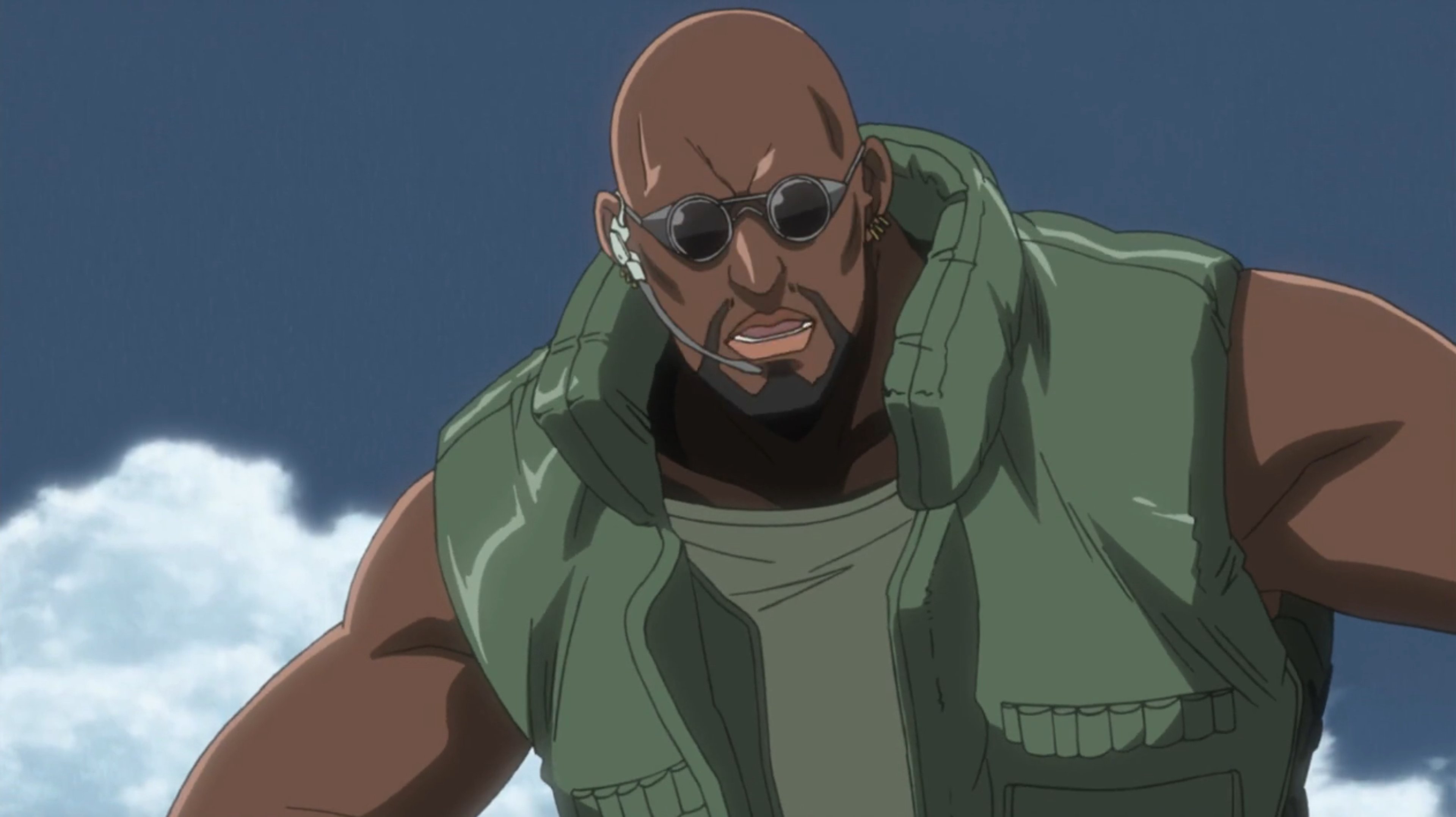 A grizzled, muscular man with a beard wearing a green military jacket and sunglasses