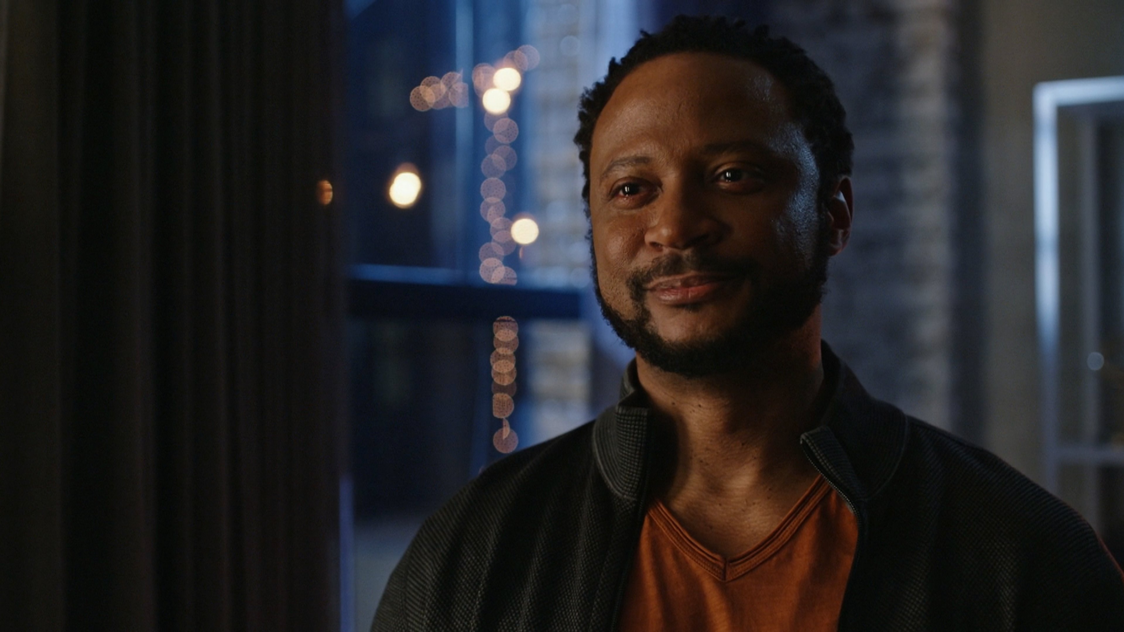 A middle-aged man with a muscular build in a dark jacket, standing in an urban setting at night.