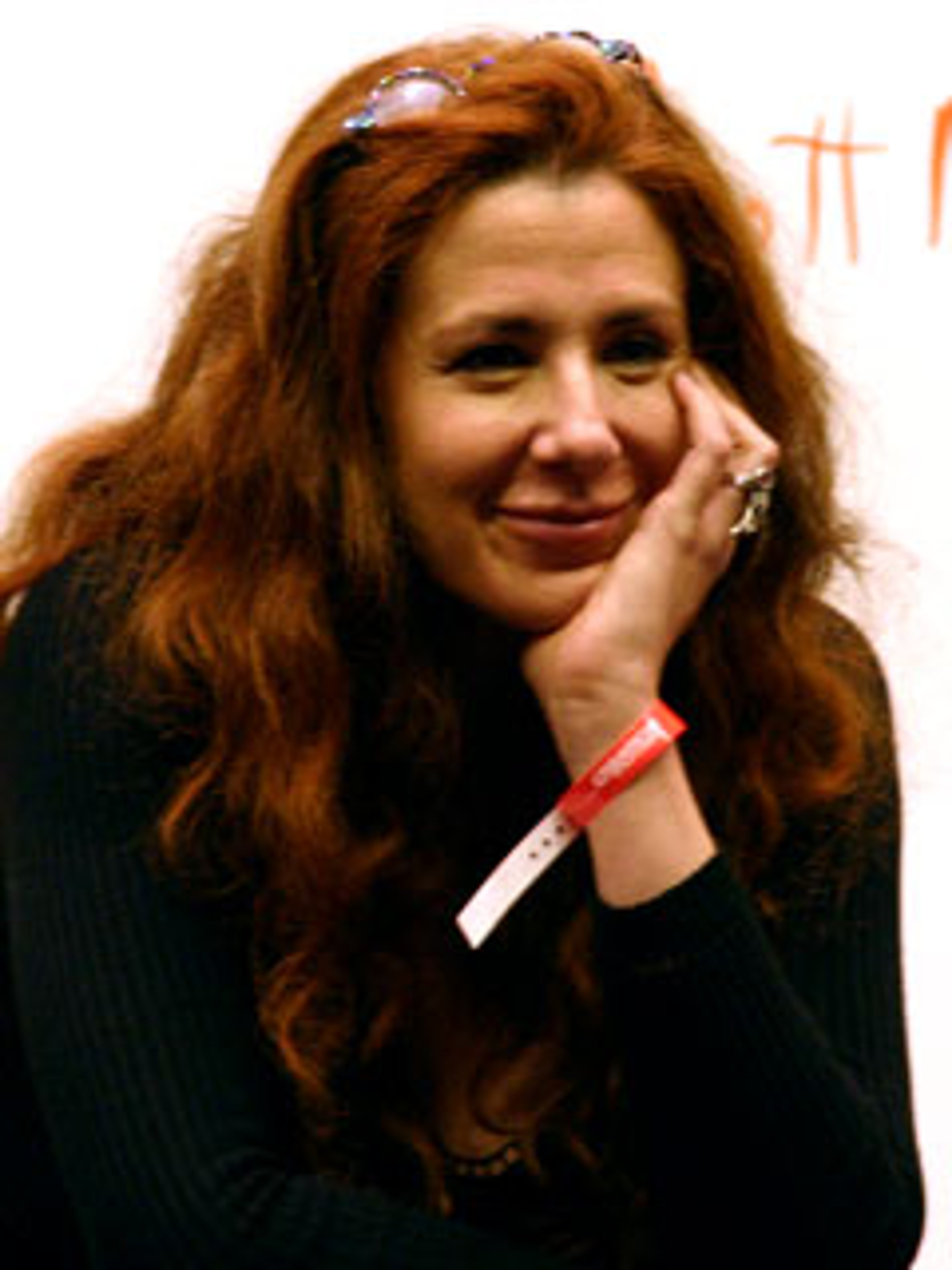 A middle-aged woman with long, wavy red hair smiling in a casual pose.