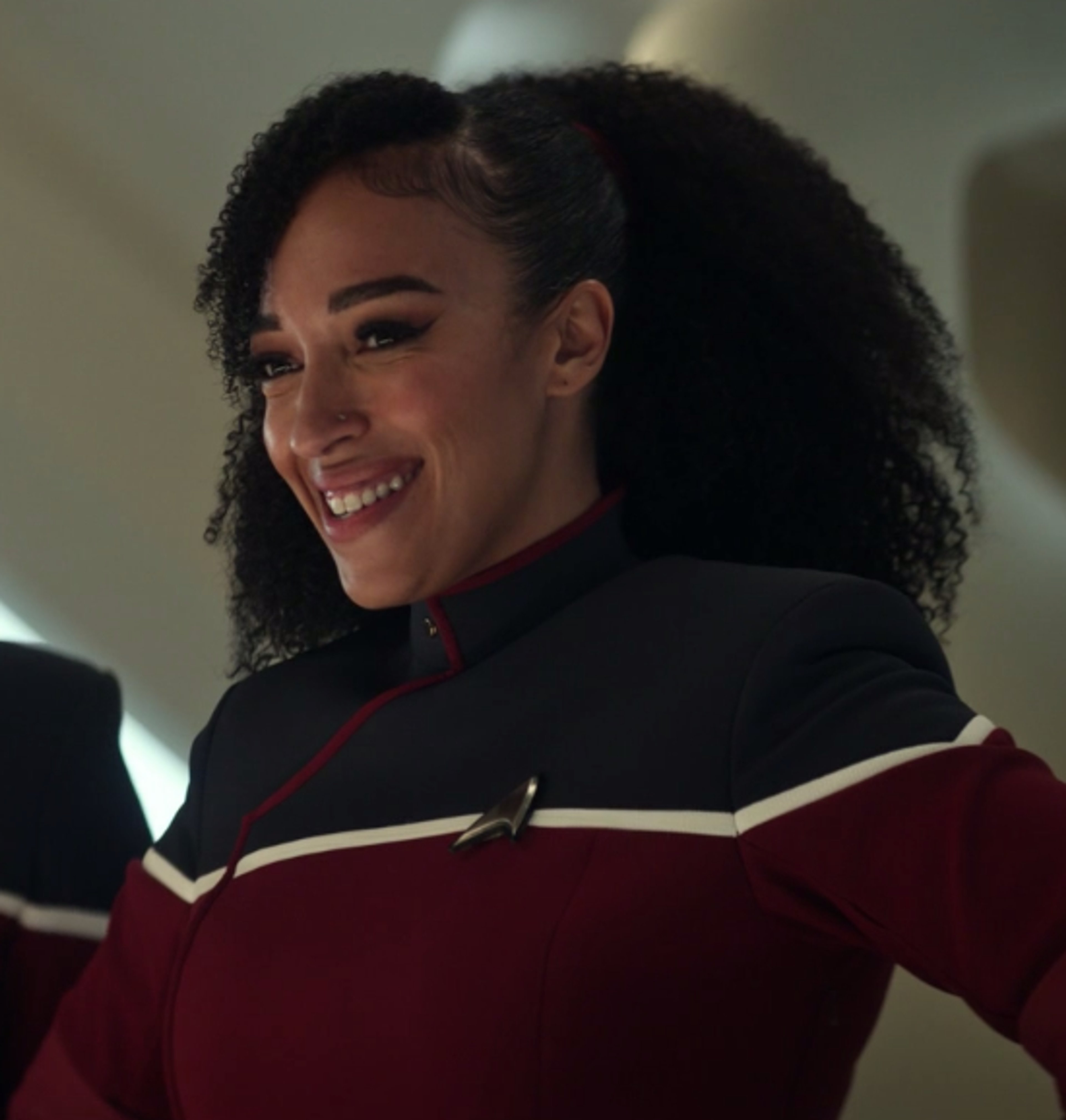 A woman in a Starfleet uniform with curly dark hair and a friendly smile