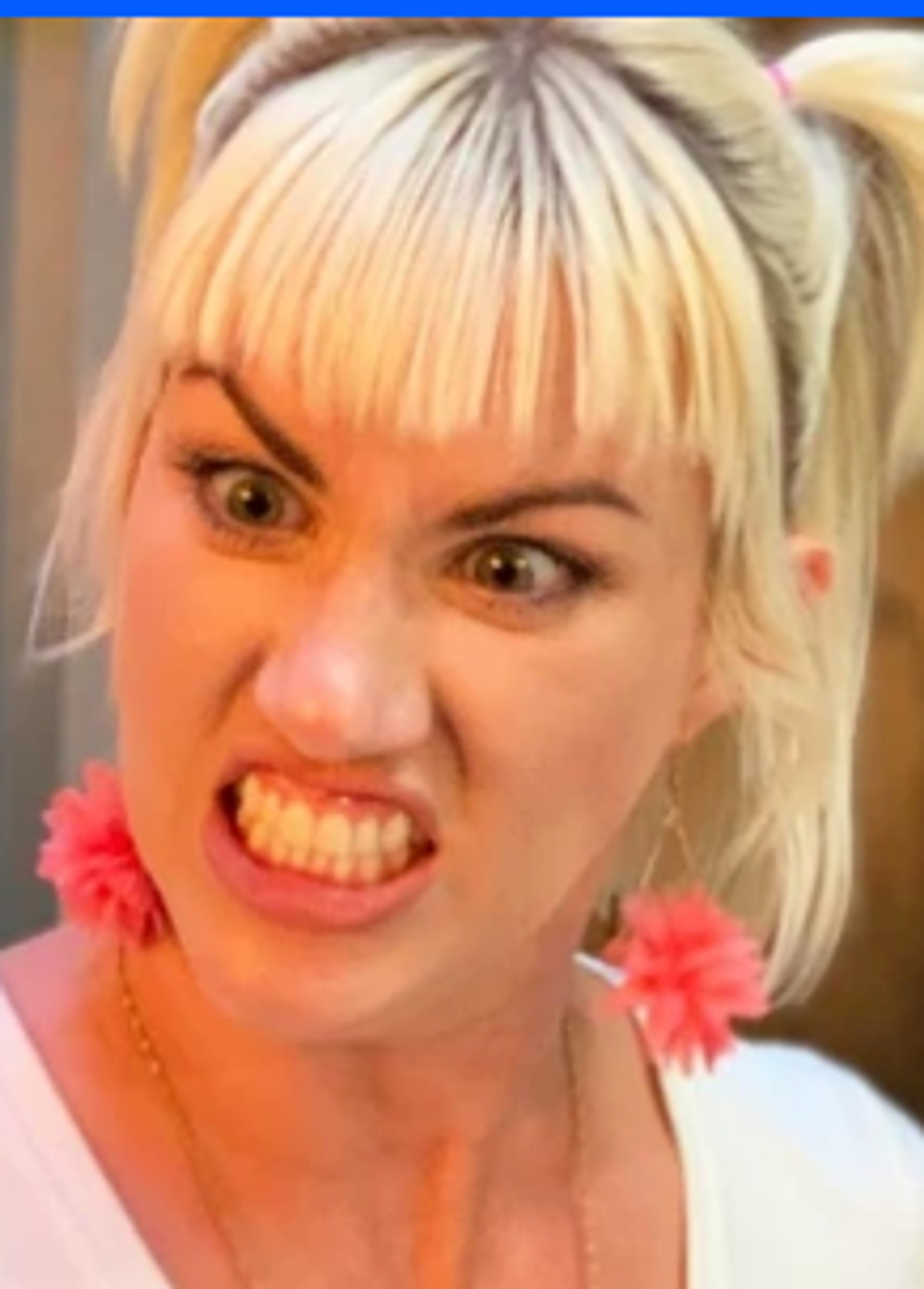 A woman with blonde hair and a pink flower in her hair making an angry, scowling facial expression.