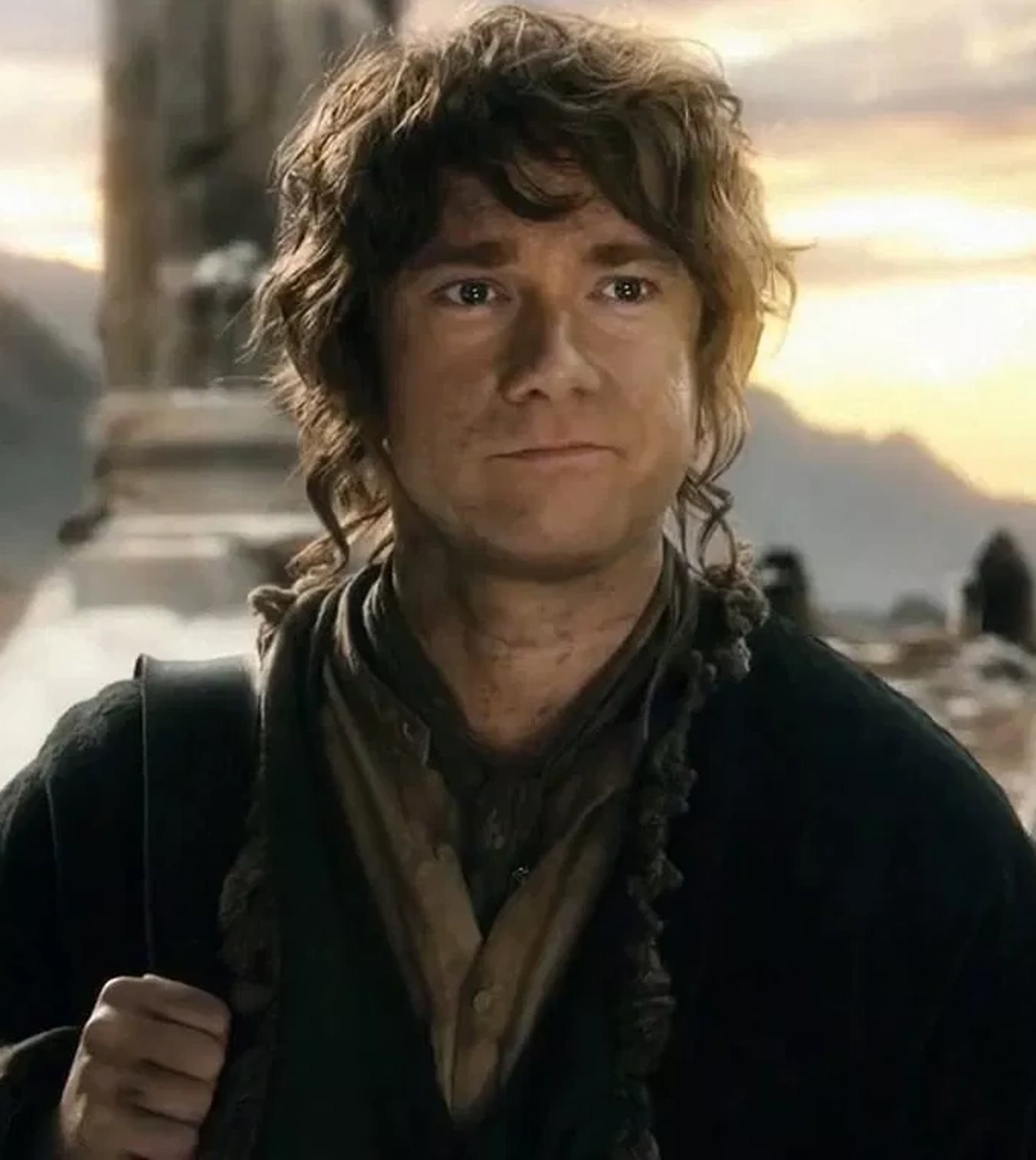 A middle-aged man with curly brown hair and a beard, wearing a brown coat and scarf, with a friendly expression on his face.