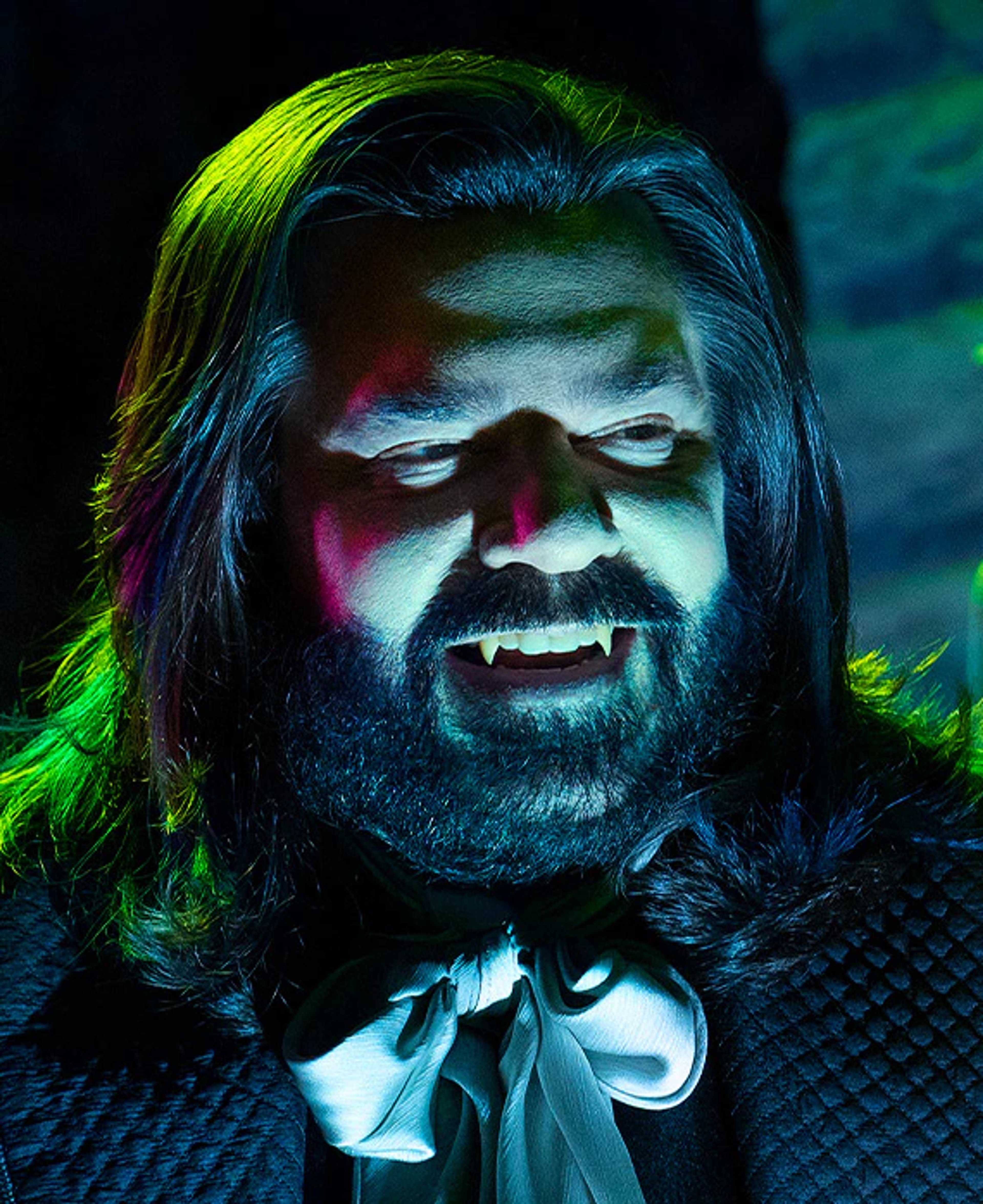 A vampire character with long dark hair, a thick beard, and glowing red eyes, wearing a black suit and tie.