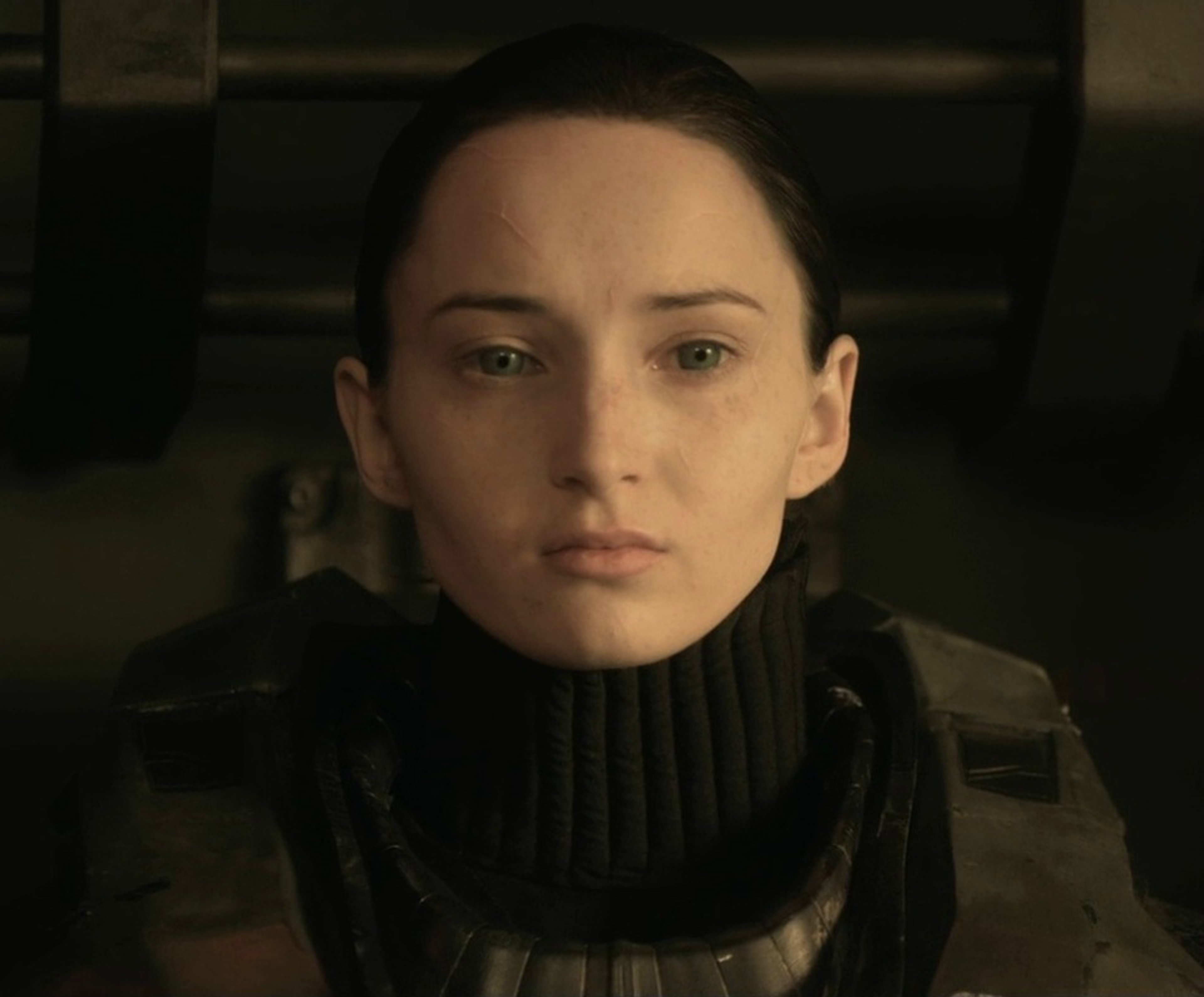 A close-up portrait of a serious-looking woman with dark hair wearing a black turtleneck sweater.