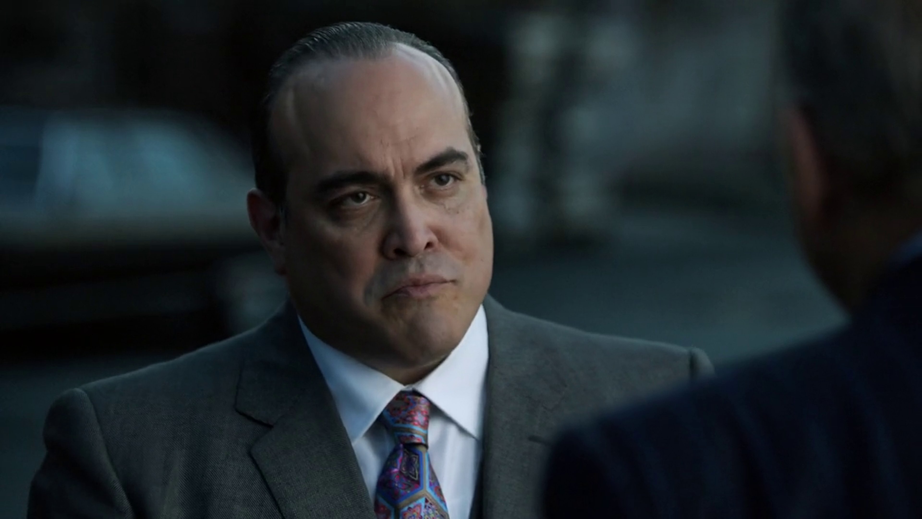 A serious-looking middle-aged man in a dark suit, likely a crime boss or other powerful criminal figure.