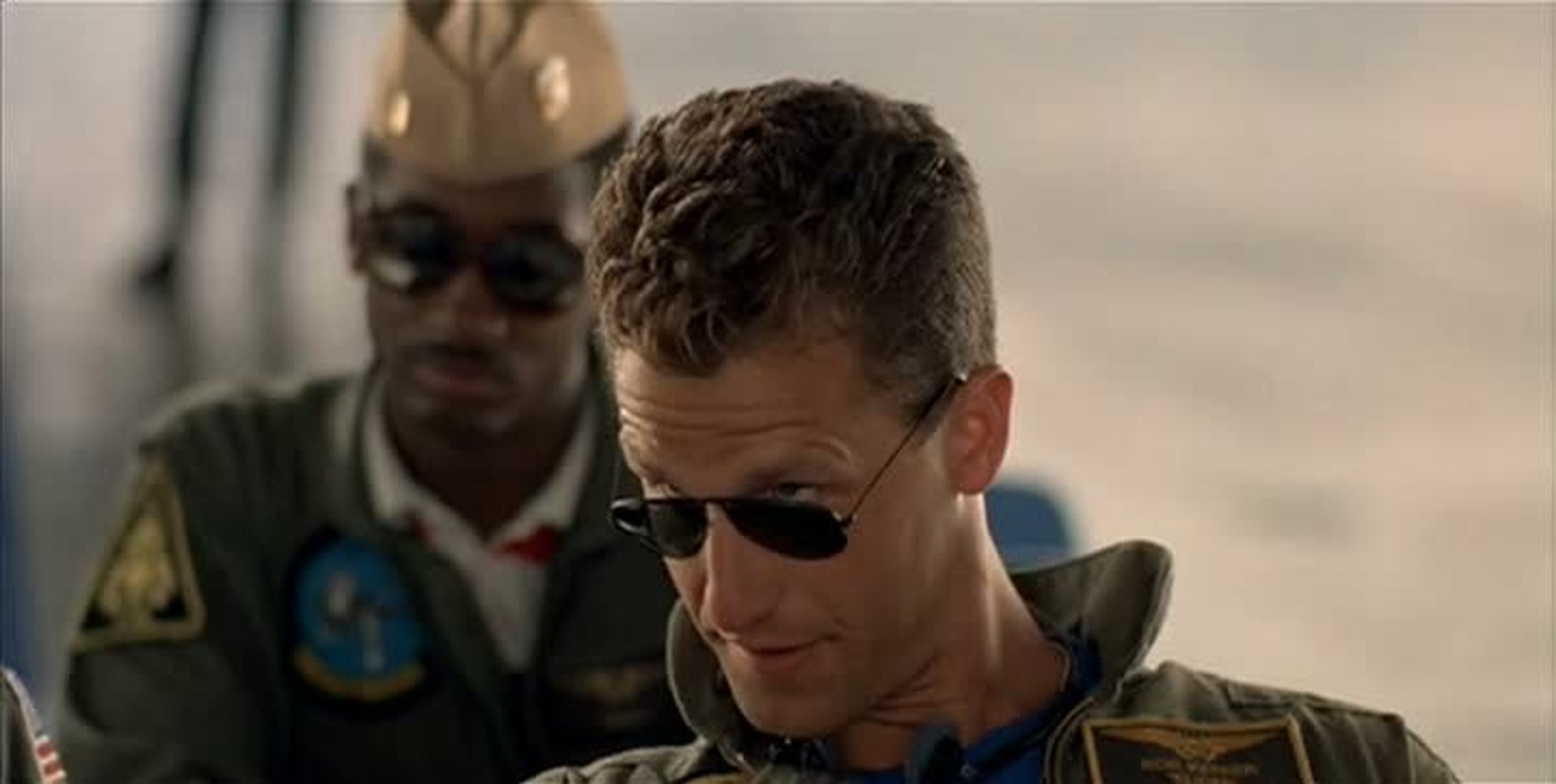 A man in a flight suit with sunglasses, looking confident.