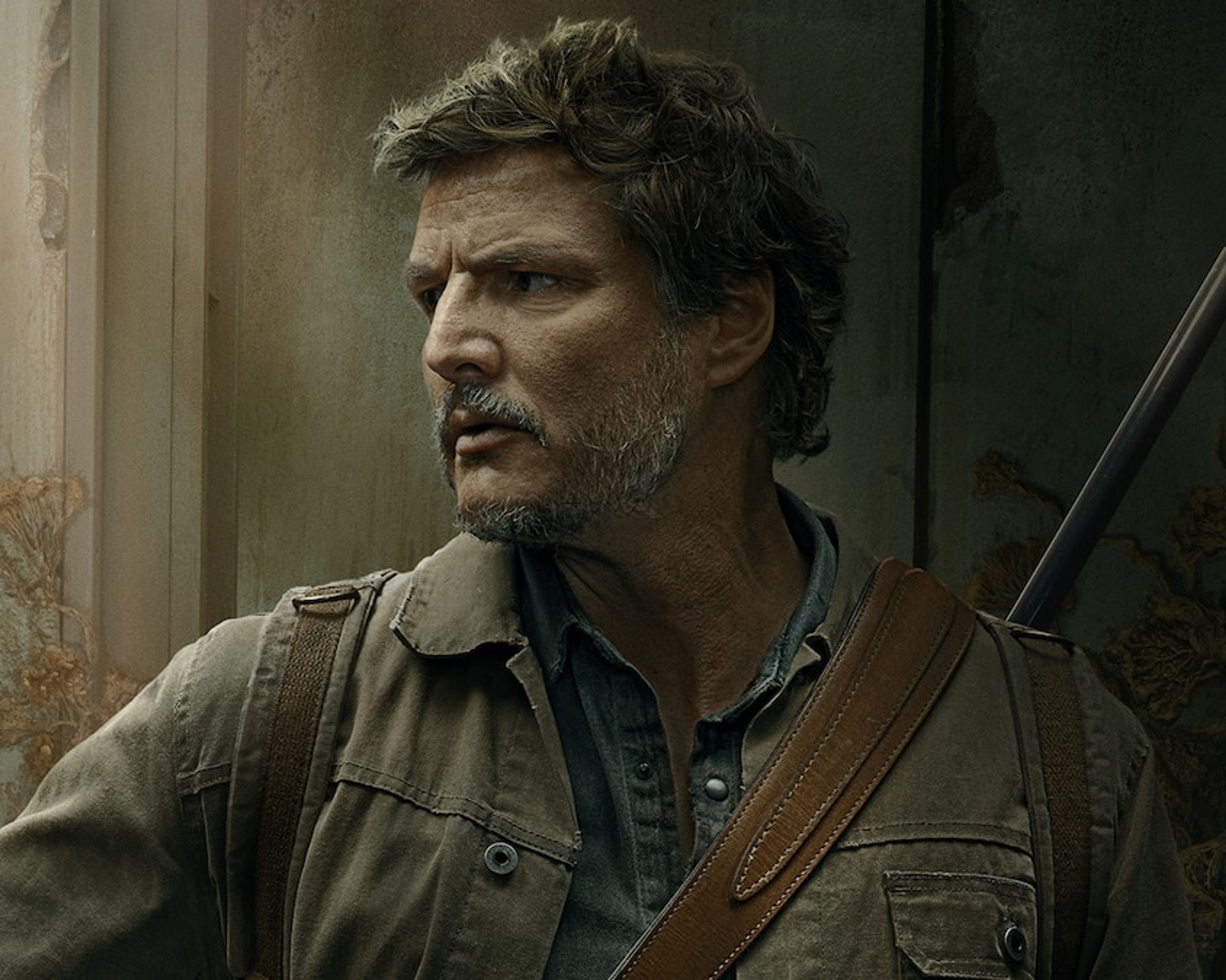 A middle-aged man with a rugged appearance, wearing a tan jacket and backpack, with a serious expression on his face.