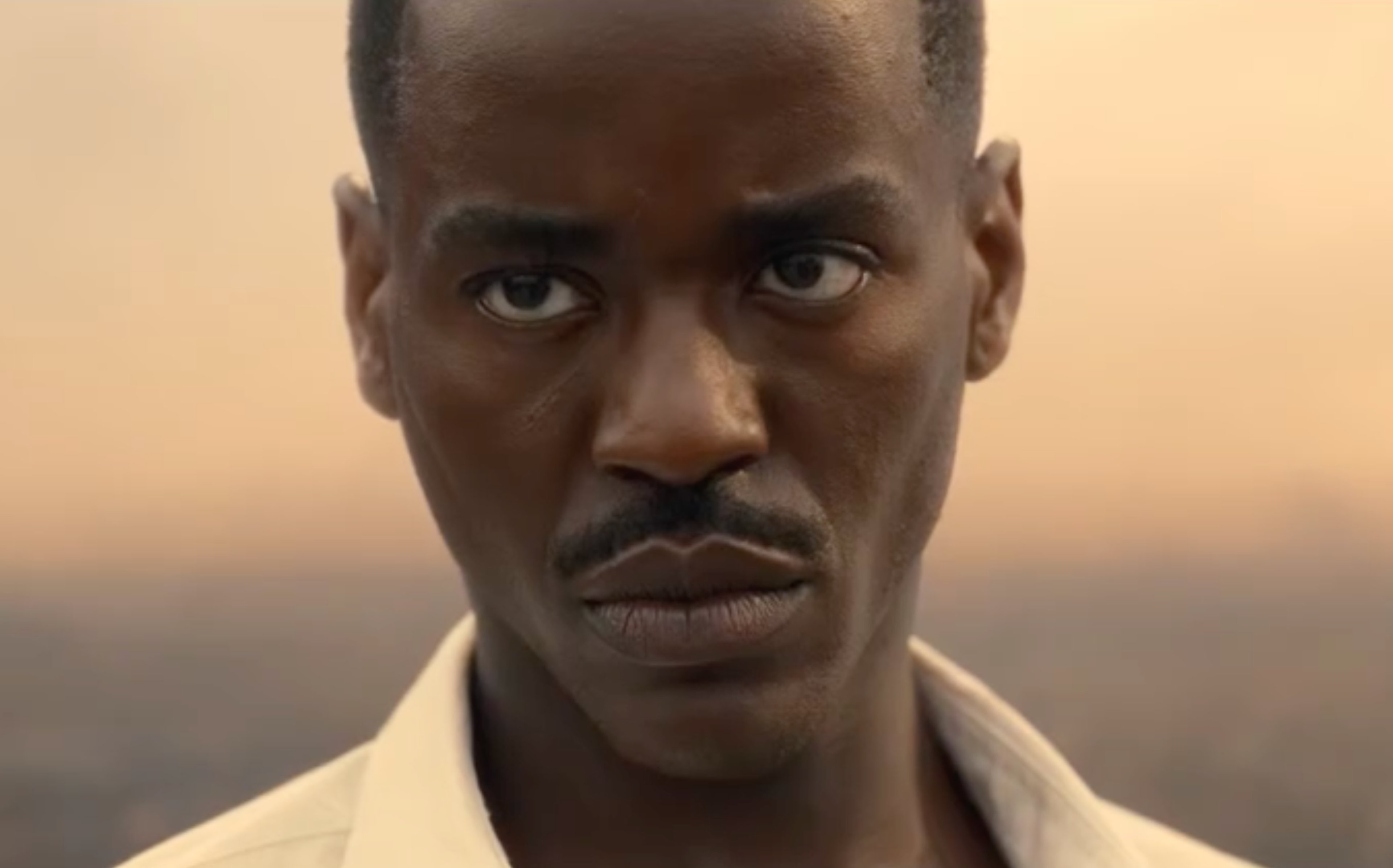 A close-up portrait of a serious-looking Black man against a desert landscape background.