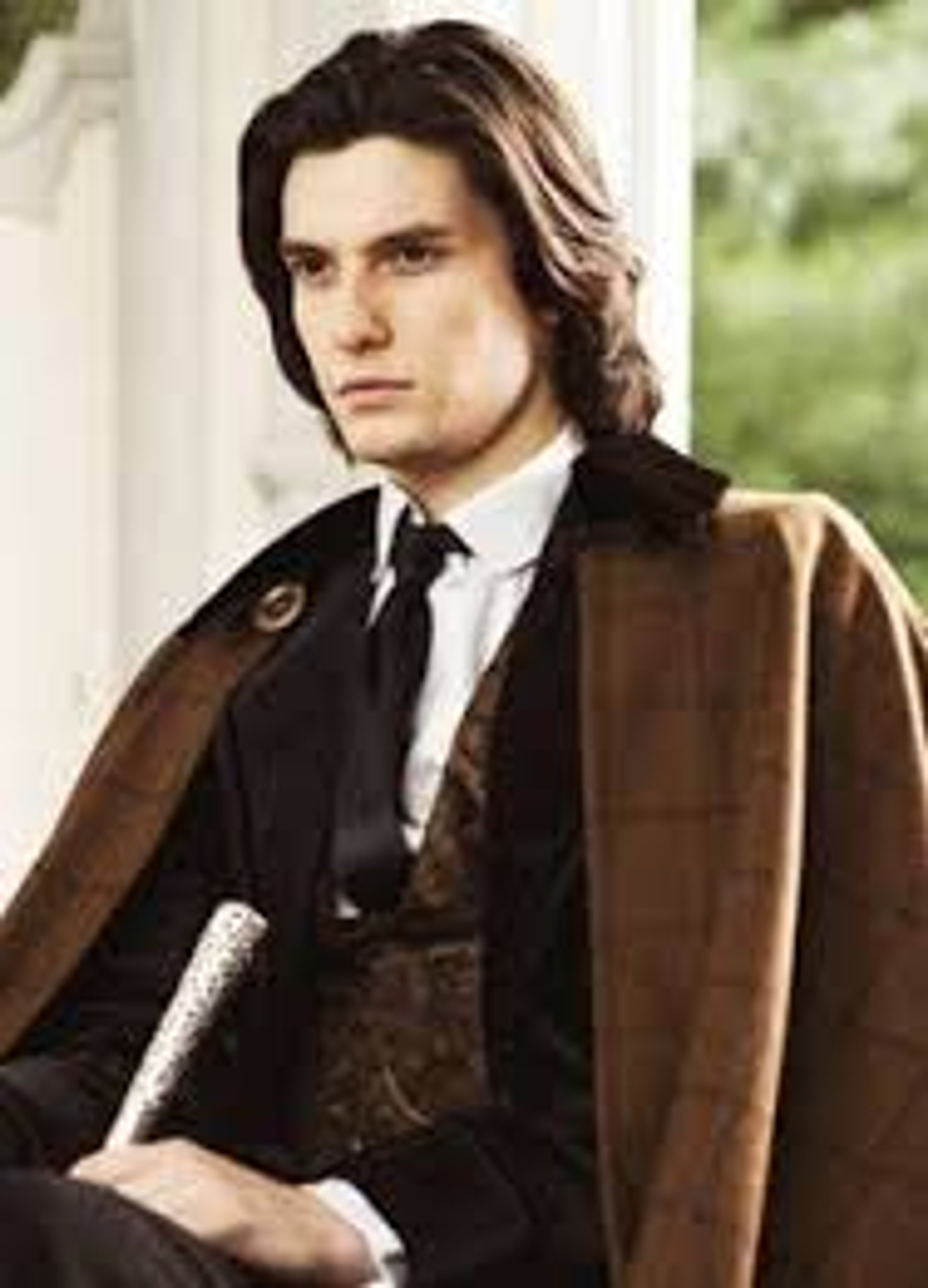 A man with long dark hair and gray eyes wearing a suit and tie