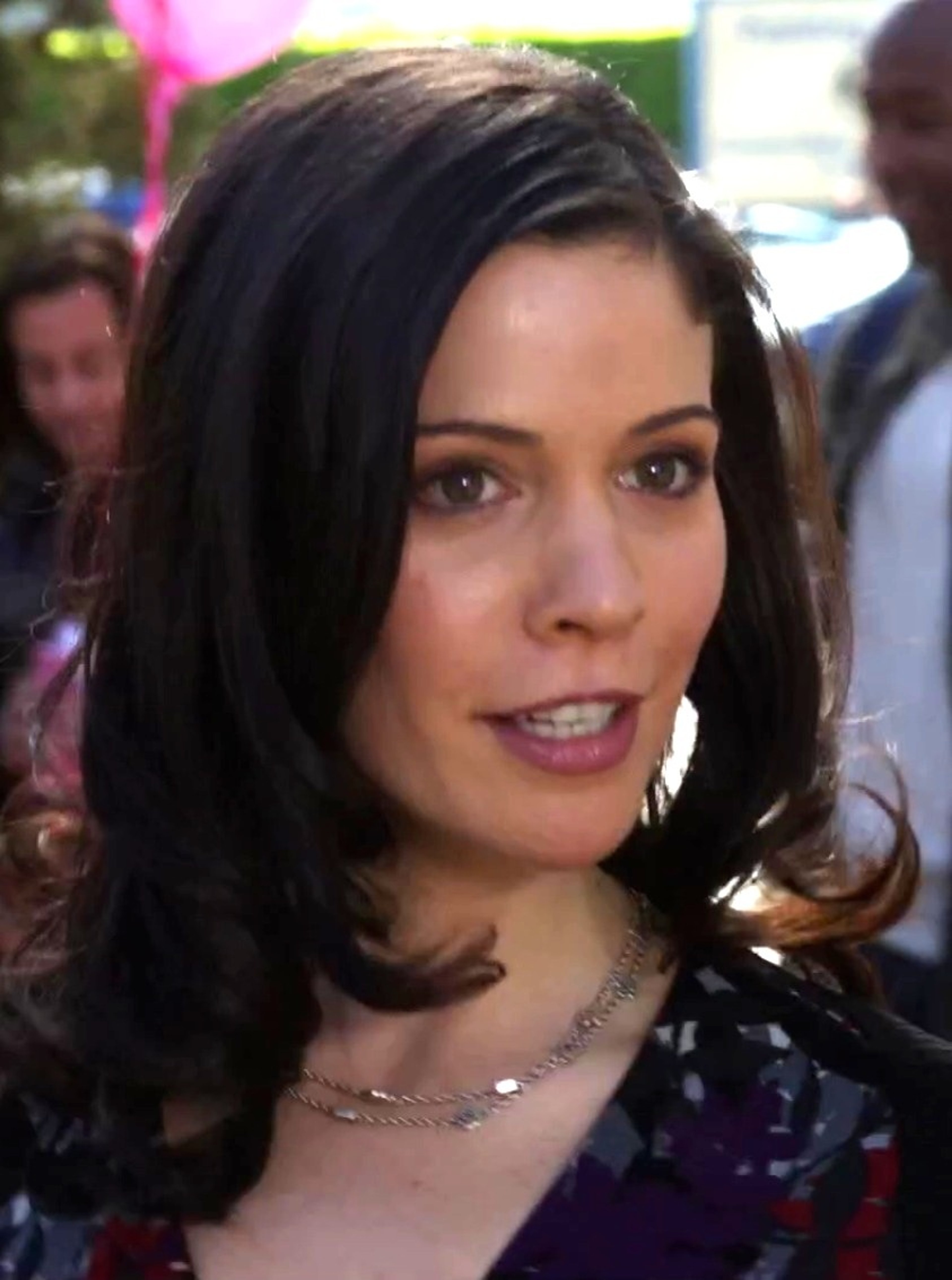 A woman with long dark hair and brown eyes, wearing a purple blouse and looking confident.
