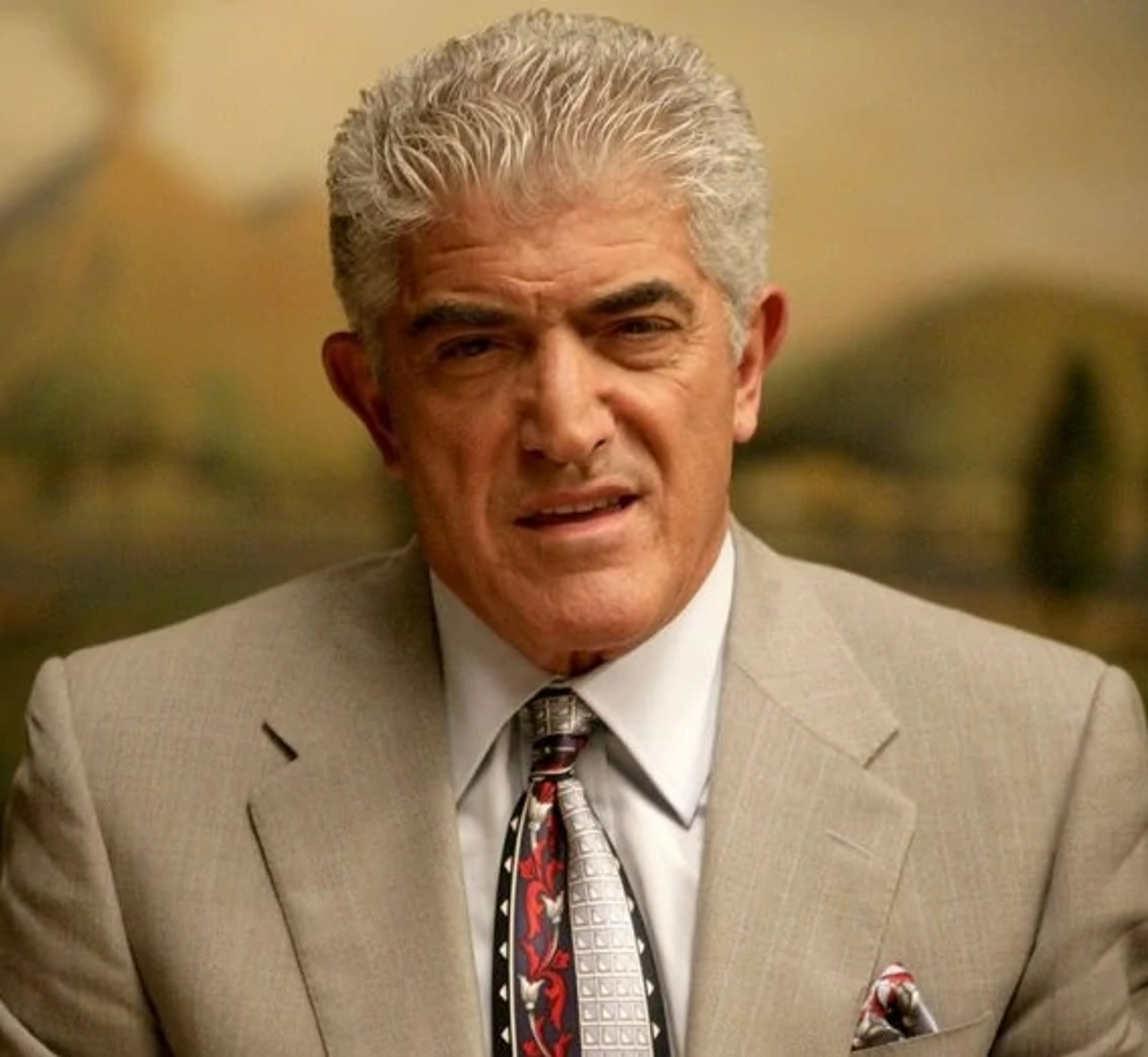 An older man with gray hair and a mustache wearing a suit and tie, with a serious expression on his face.
