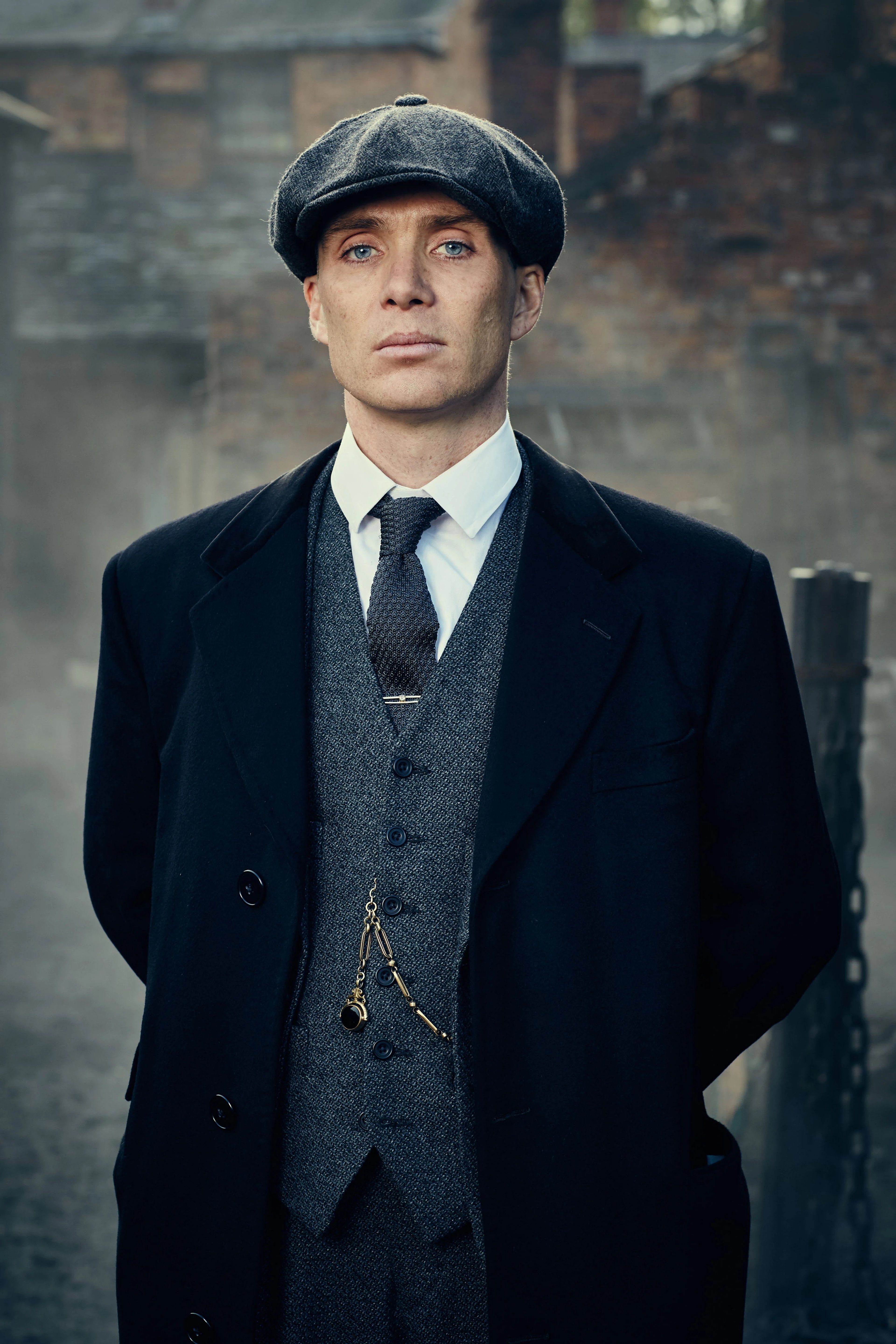 A man in a black suit and hat standing in front of a brick wall