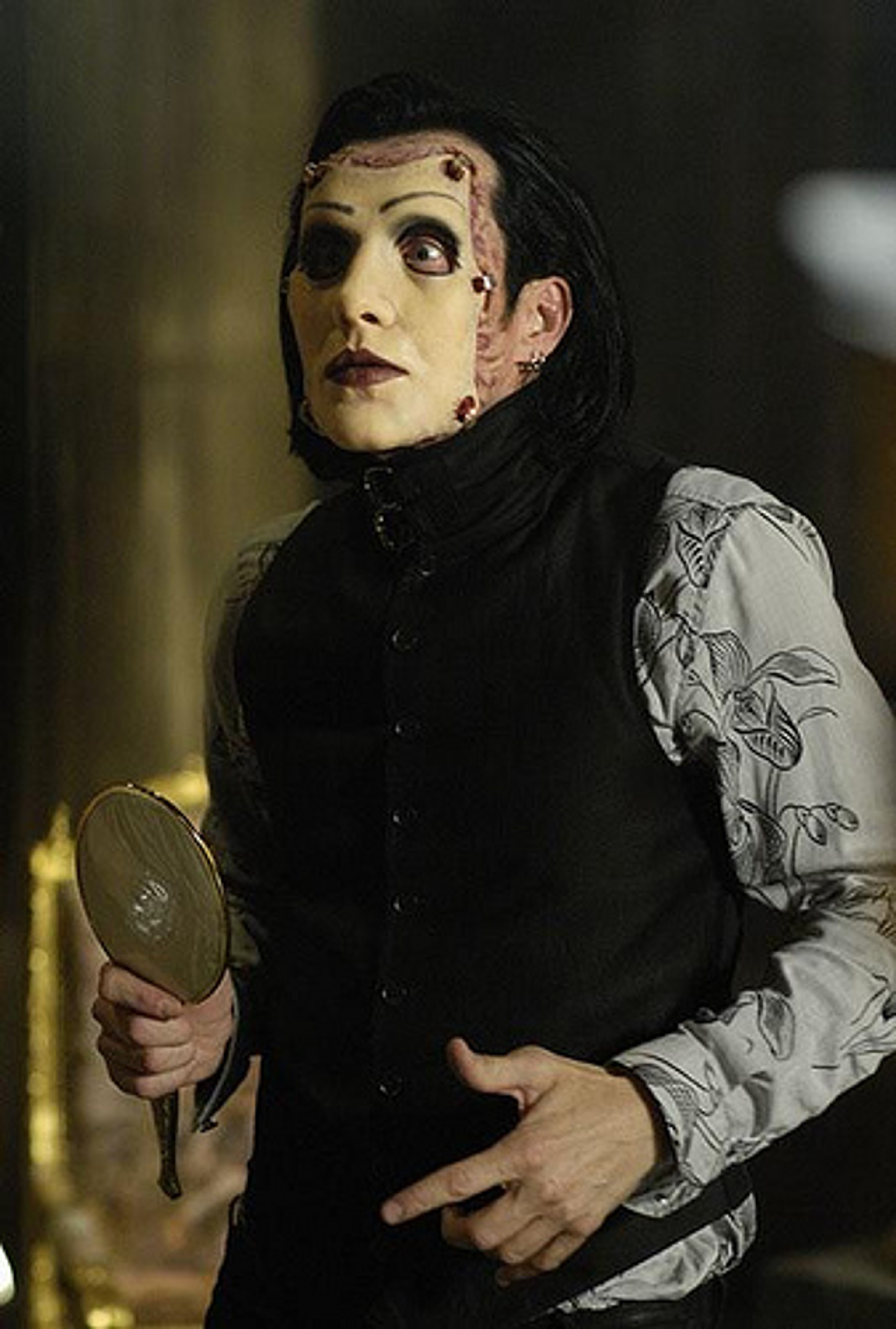 A character with a scarred face wearing a surgical mask and holding a hand mirror