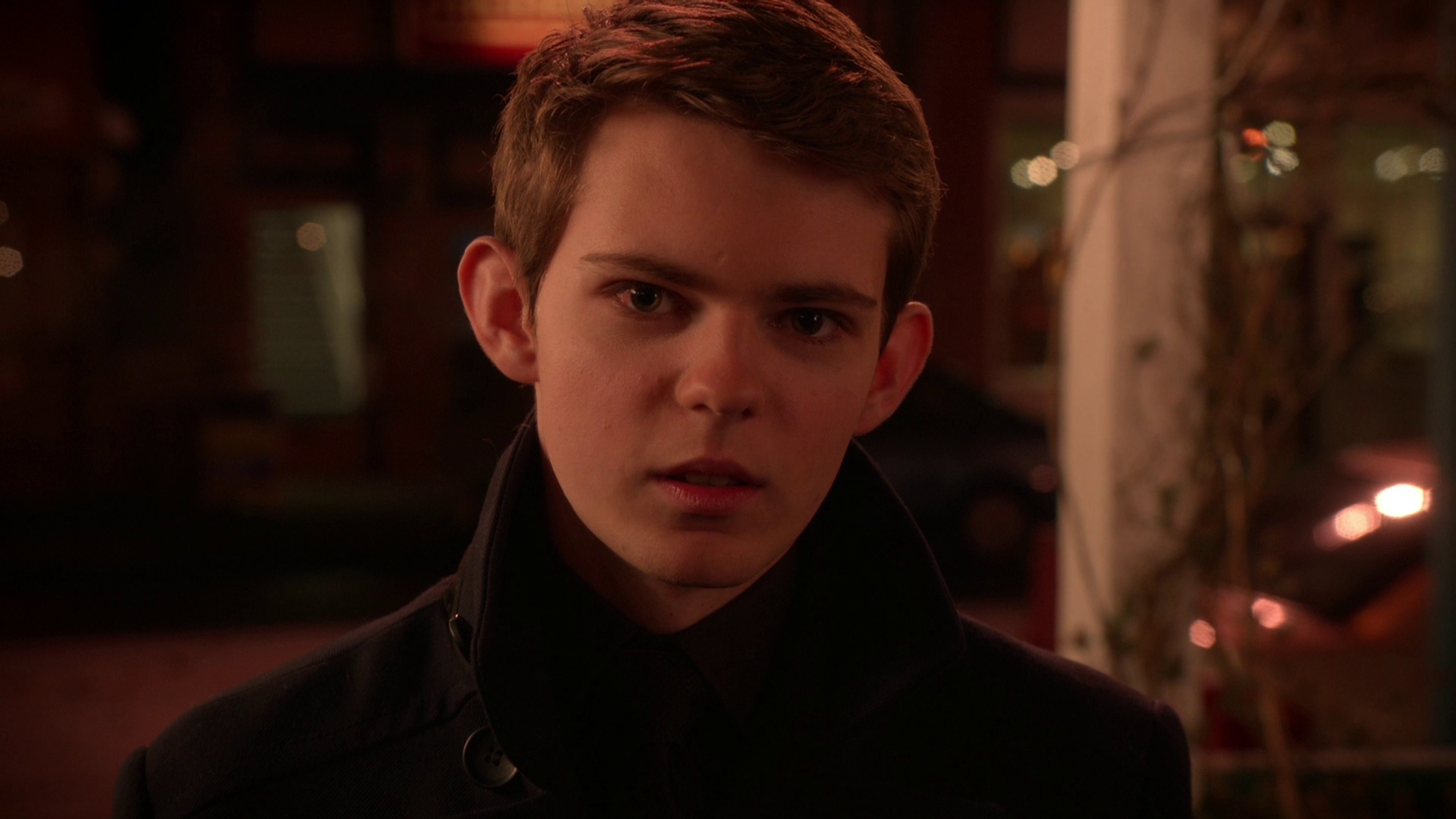 A young man with short brown hair in a serious expression, wearing a dark jacket.