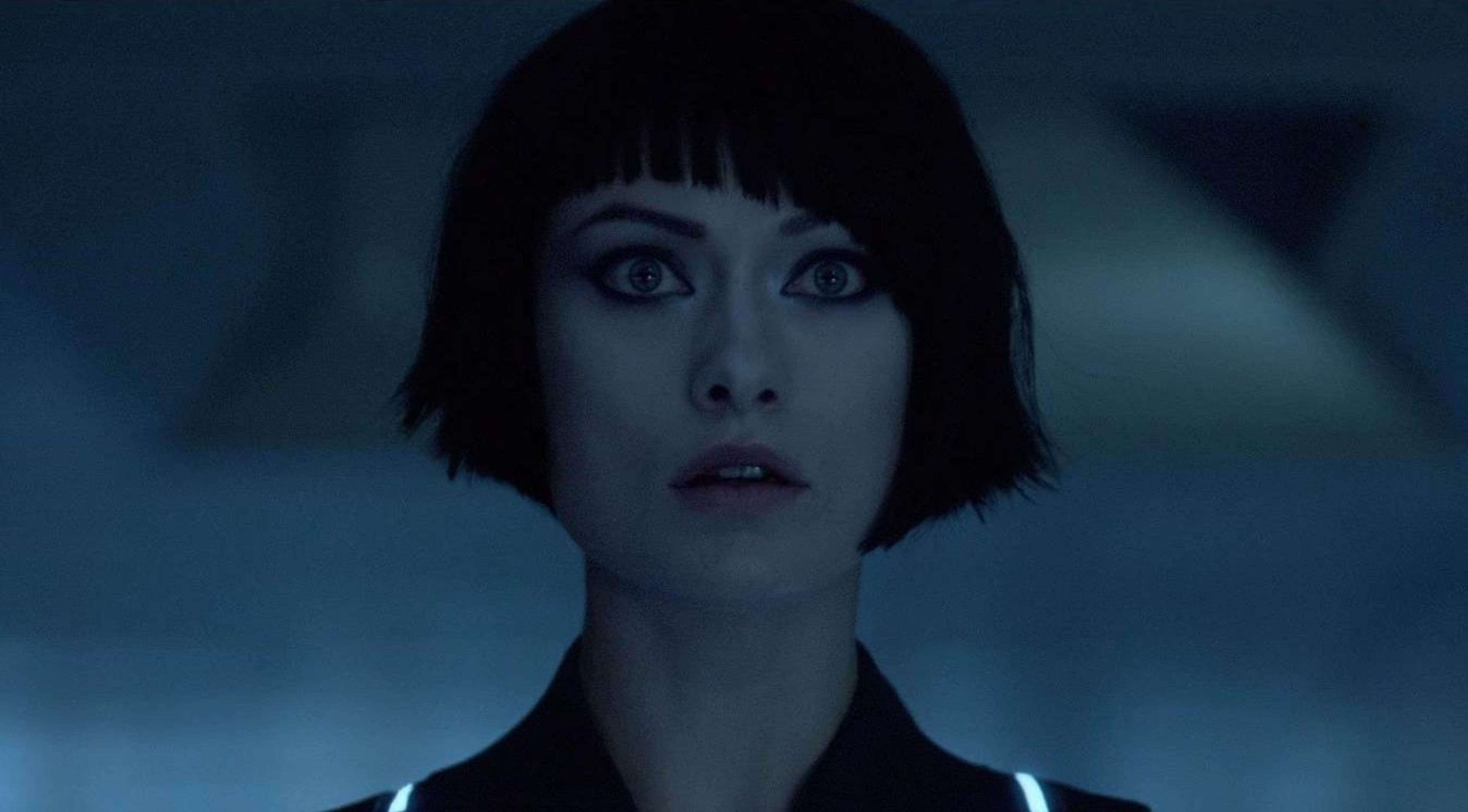 A young woman with short dark hair and blue eyes wearing a black futuristic uniform, with a serious expression on her face.