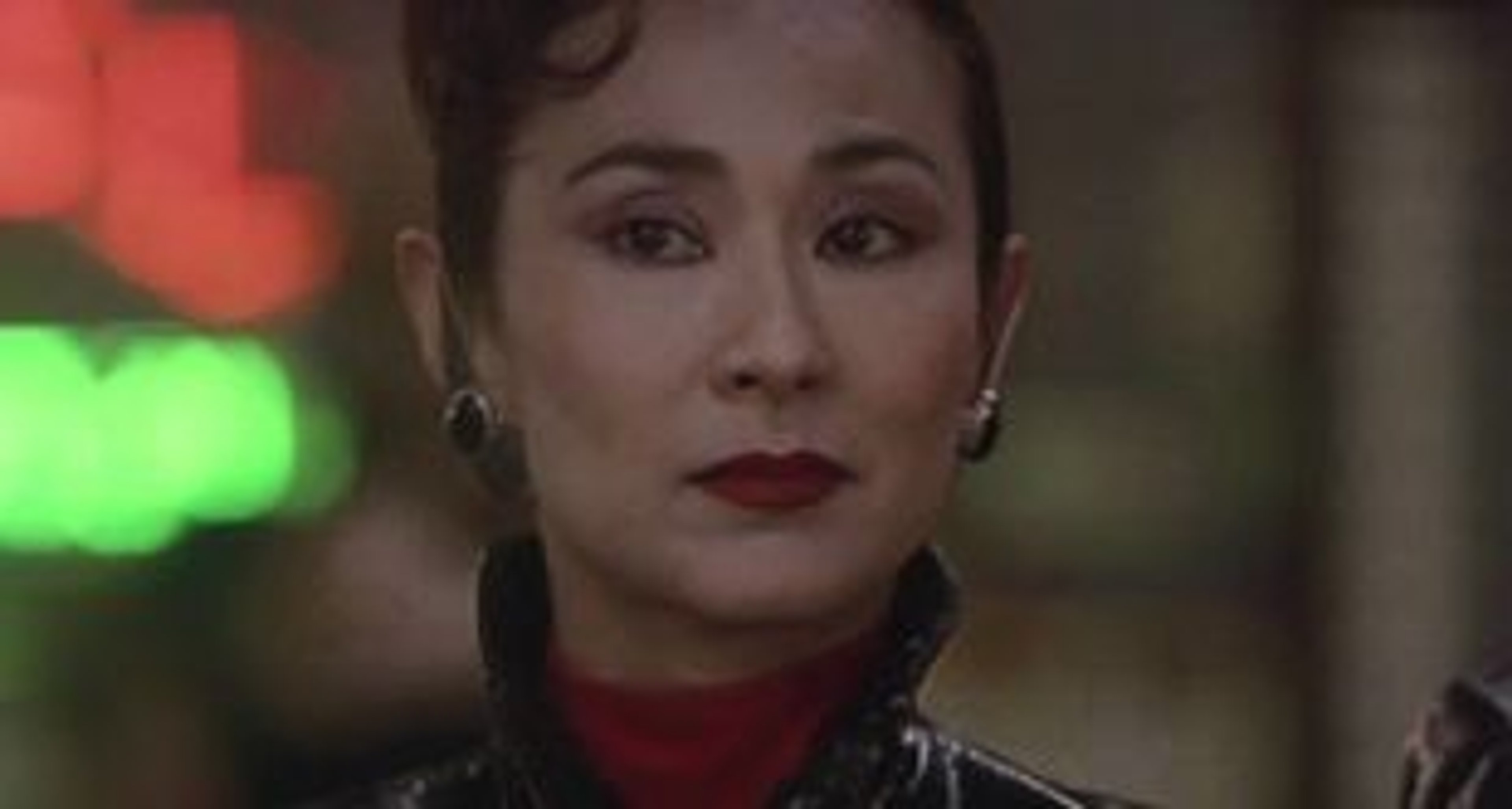 A woman with dark hair and a serious expression, wearing a red blouse.