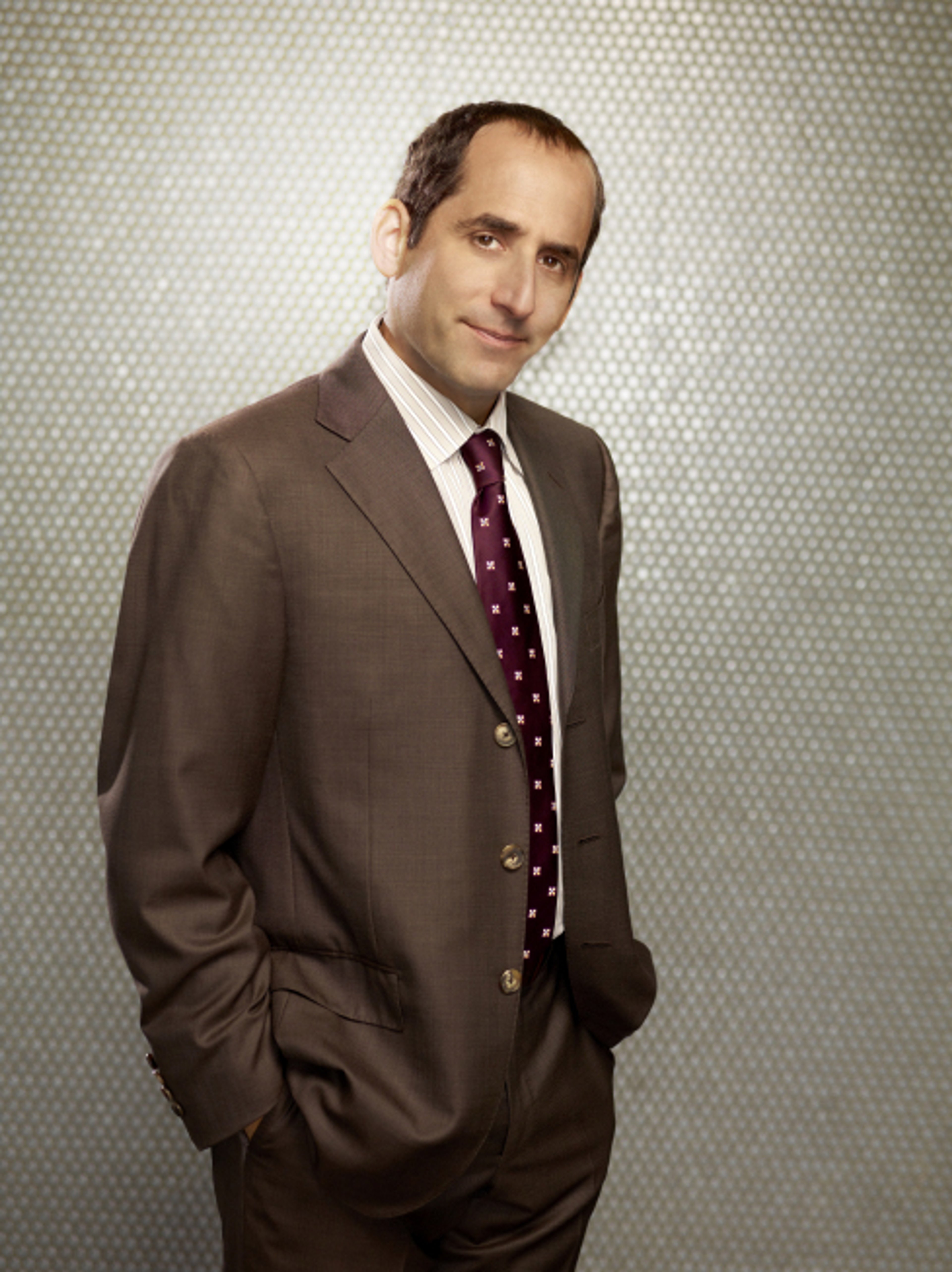 A middle-aged man in a suit and tie standing in front of a plain background