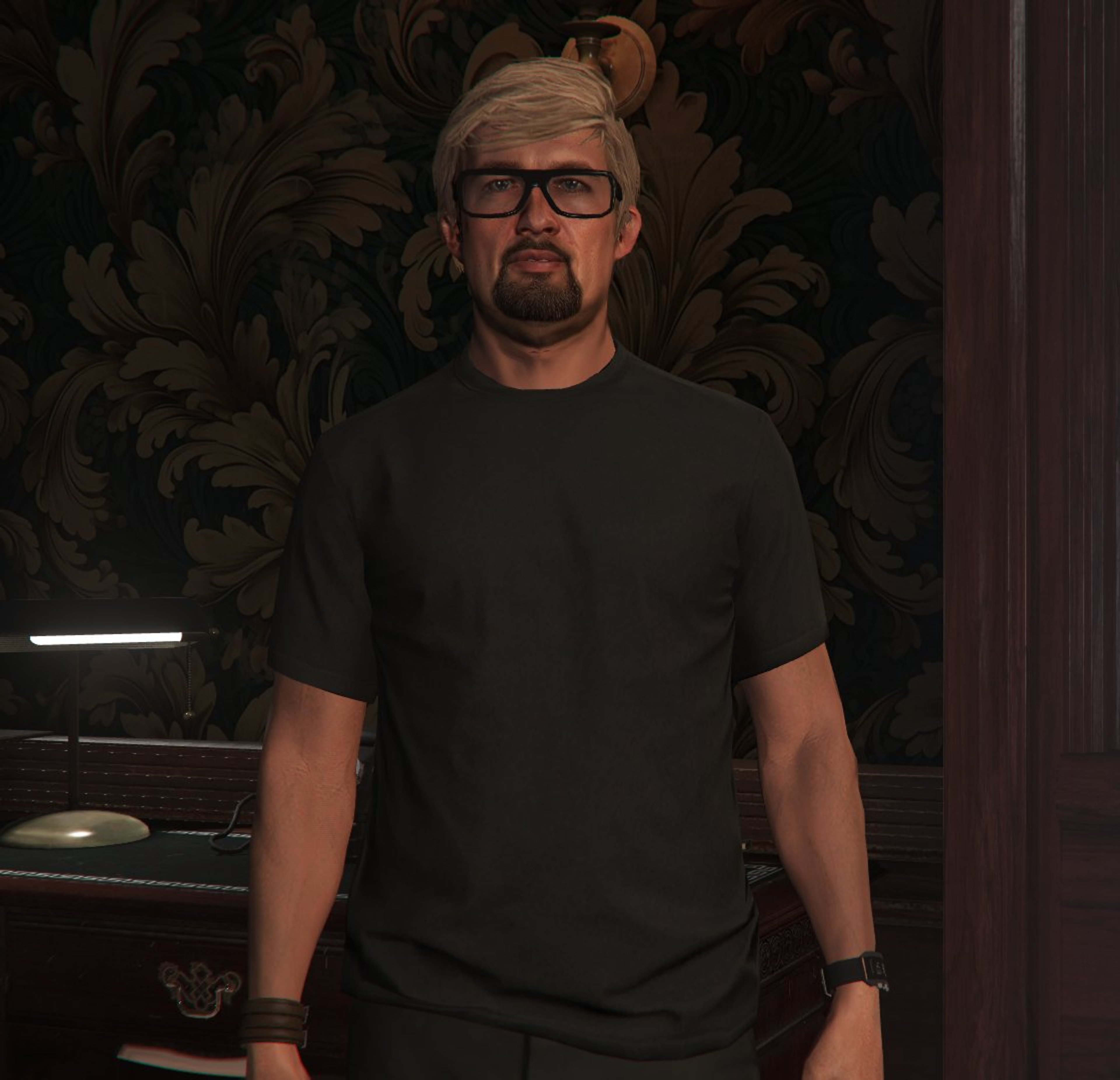 A man with short brown hair and glasses wearing a black t-shirt in a dimly lit room