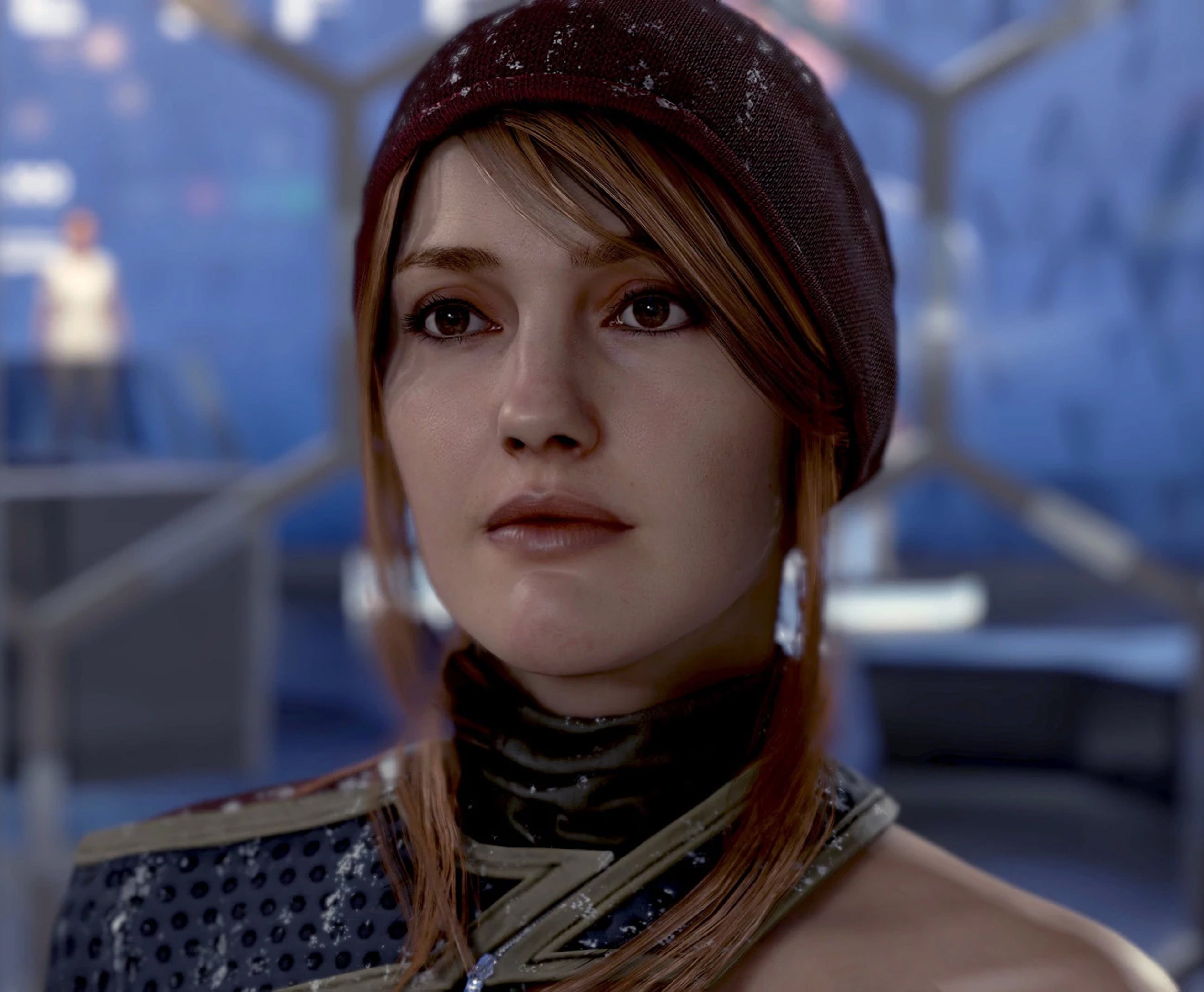 A young woman with reddish-brown hair wearing a dark jacket or coat with a high collar, in a futuristic, sci-fi setting.