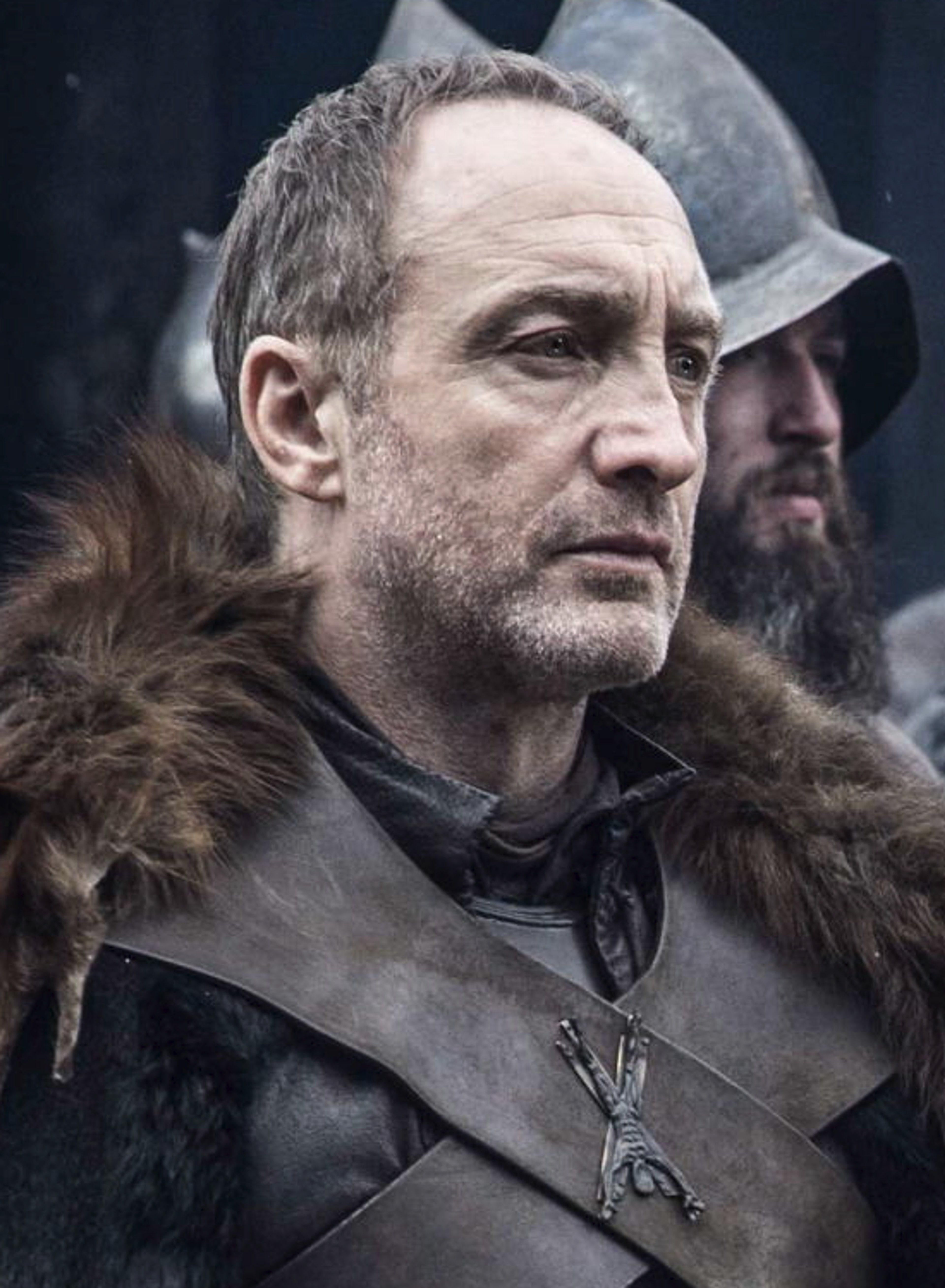 A middle-aged man with gray hair and a beard, wearing a fur-lined cloak and having a stern expression.