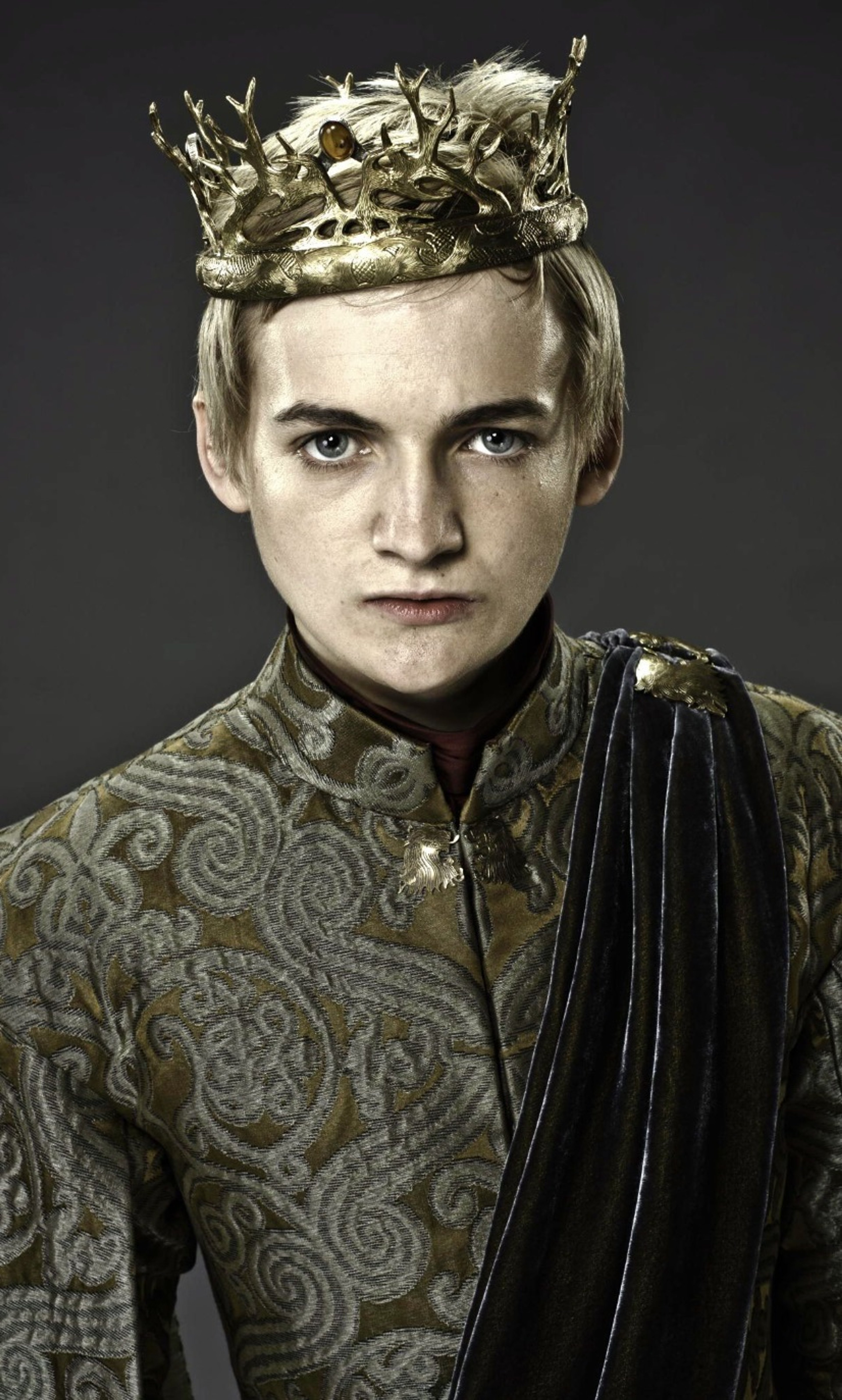 A young man wearing an ornate golden crown and patterned robe, with a stern expression on his face.