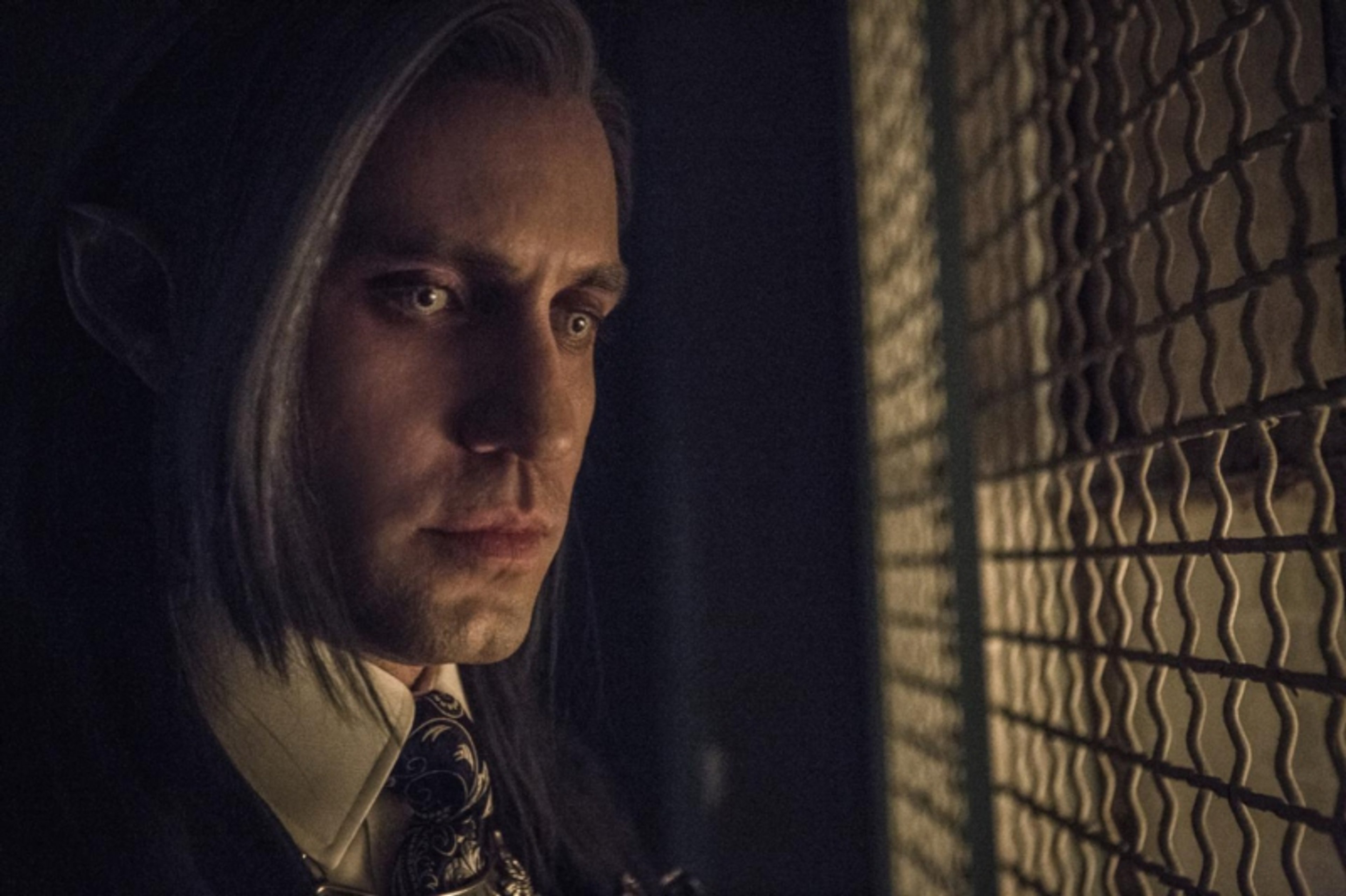 A serious-looking male character with silver-gray hair wearing a dark suit