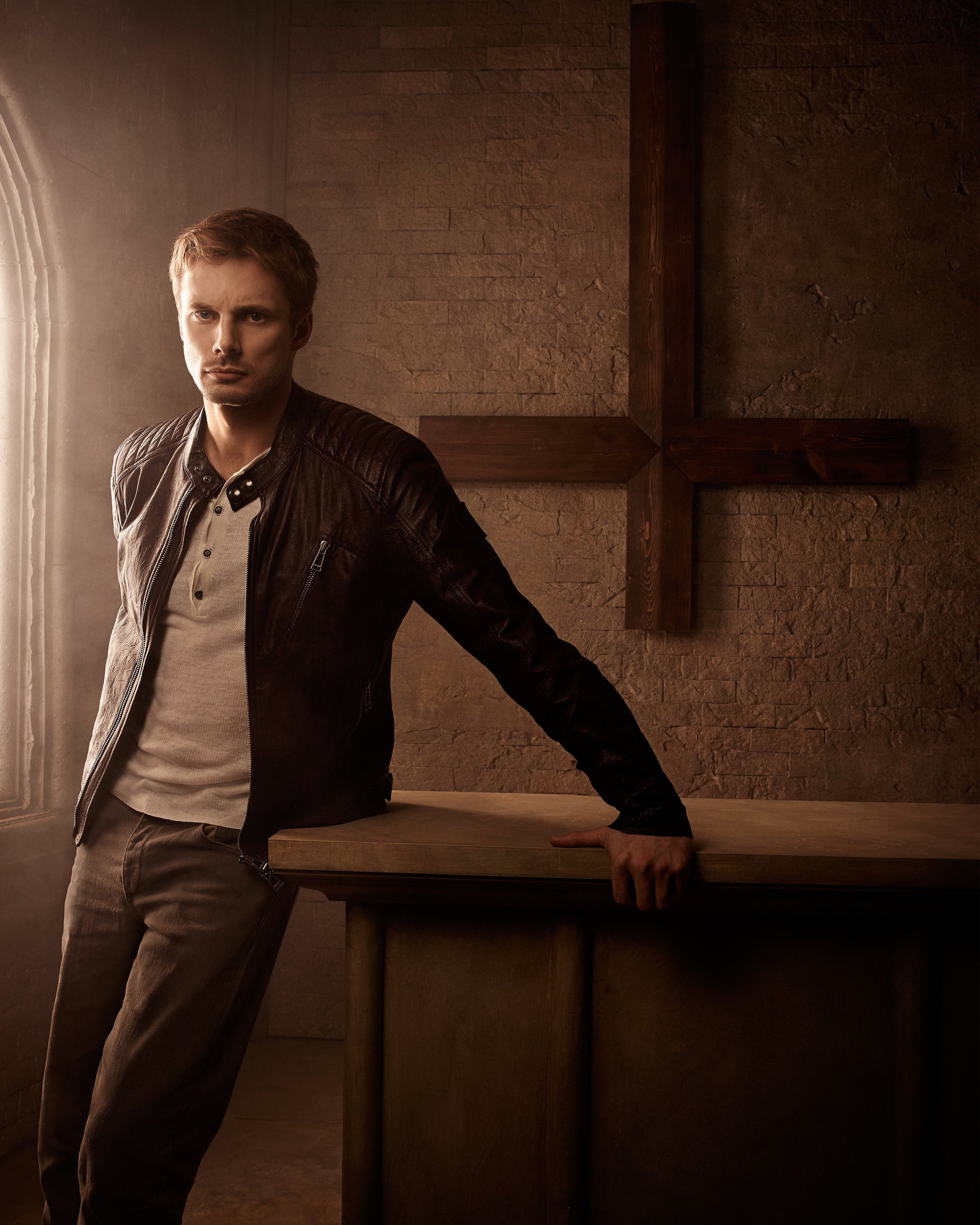 A serious-looking man with piercing eyes standing in a dimly lit interior