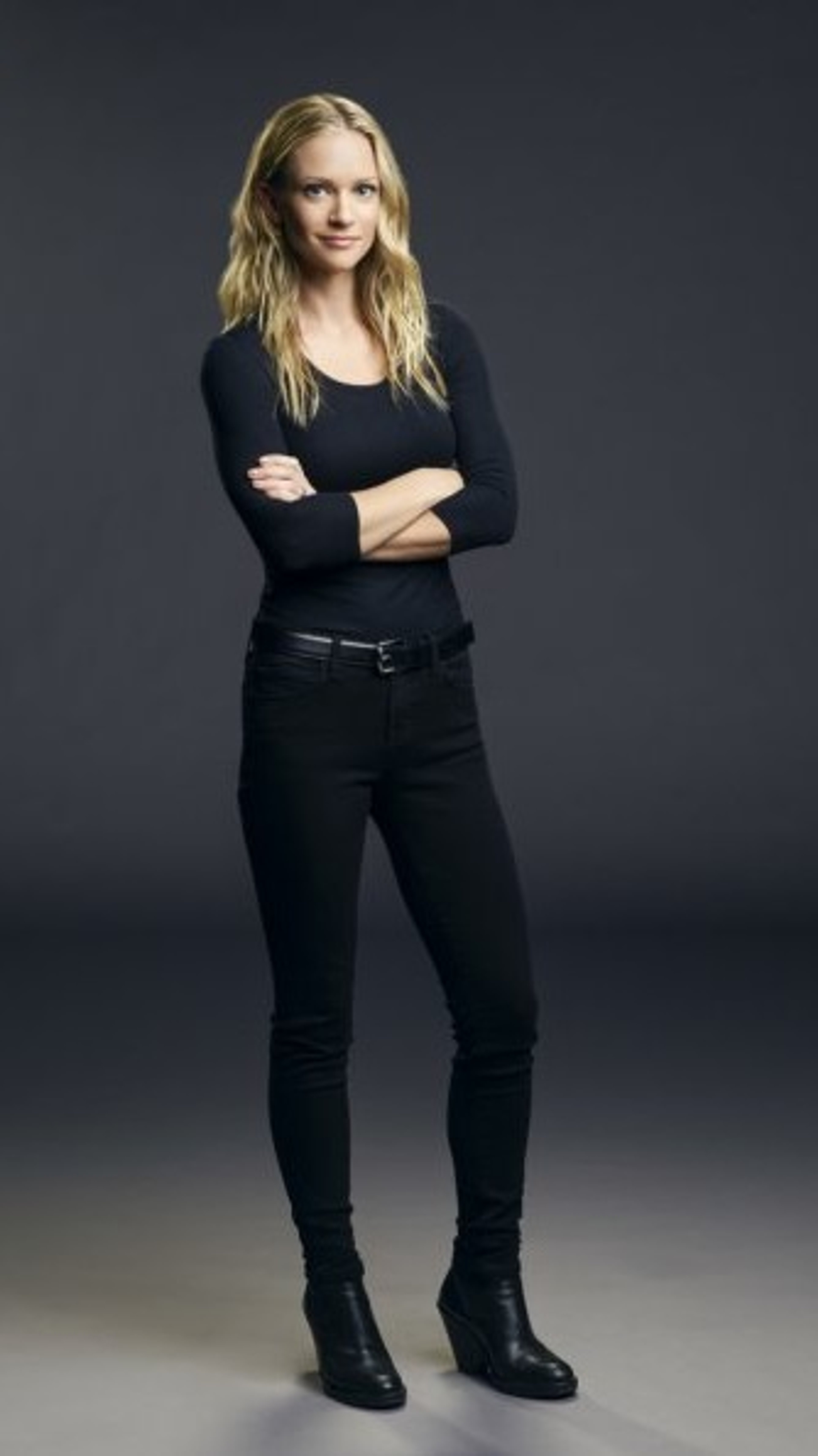 A young, blonde woman in a black outfit standing with a serious expression