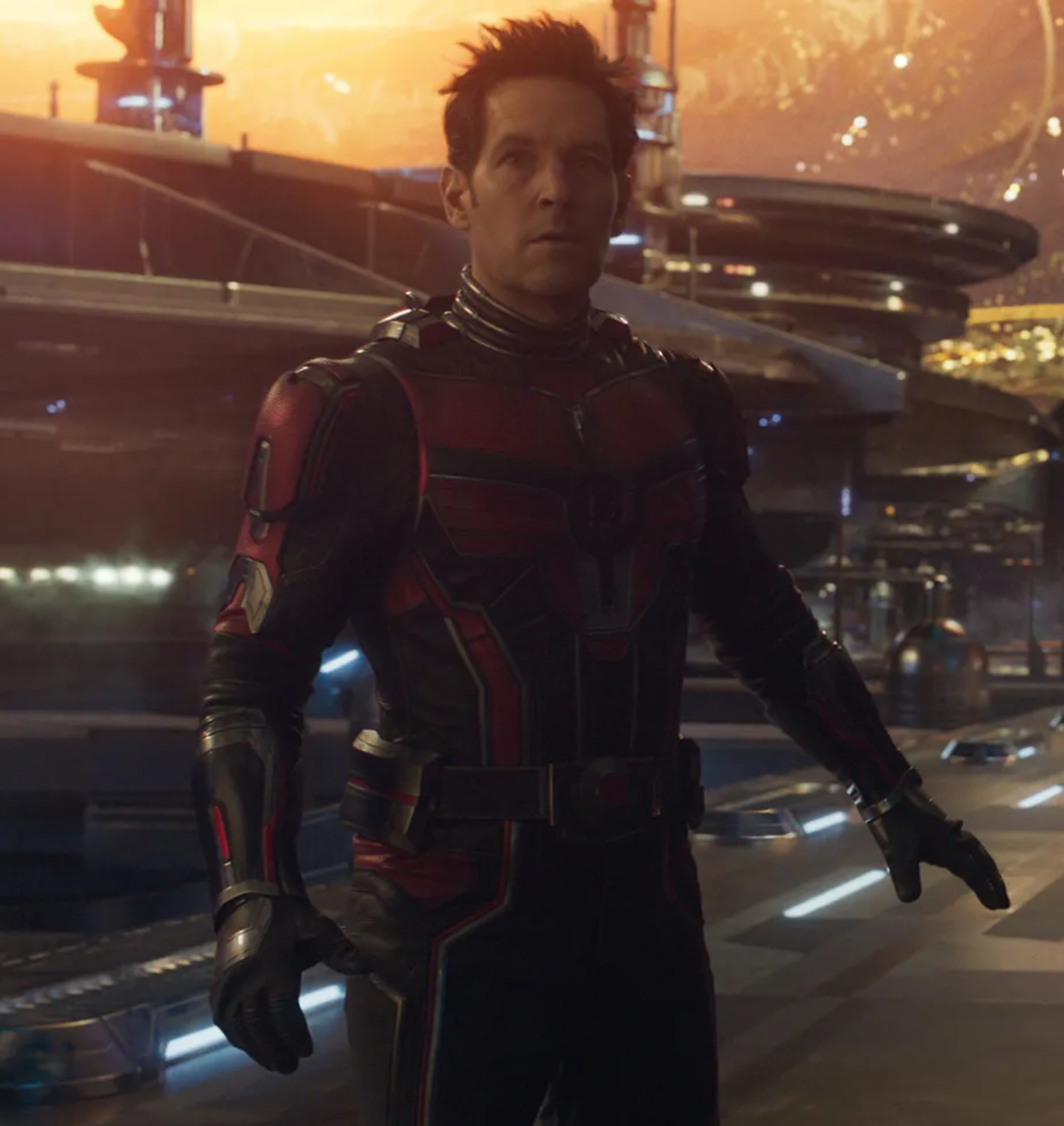 A man in a red and black superhero costume standing in front of a futuristic city skyline.