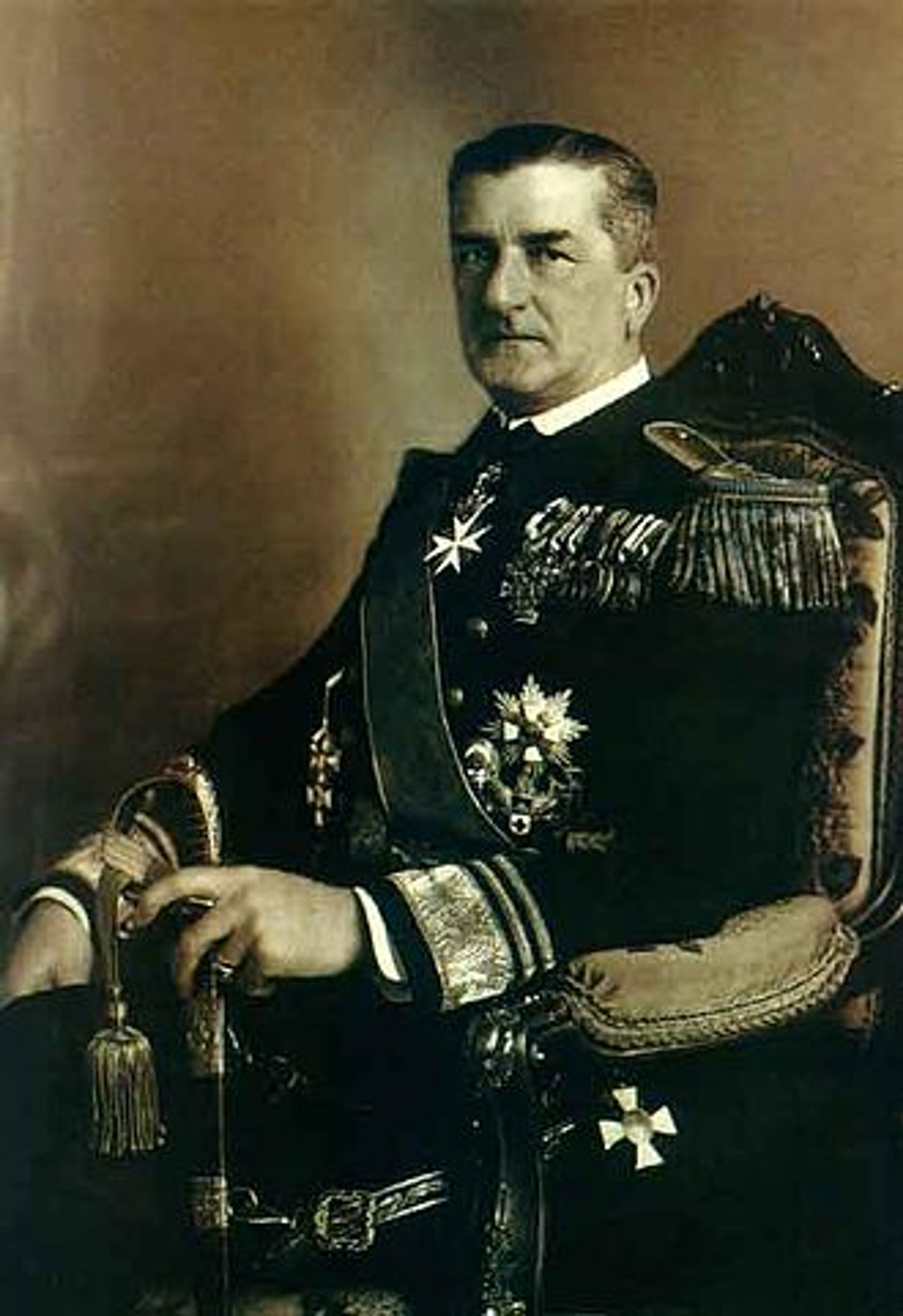 A middle-aged man in a military uniform with medals and decorations, seated in an official setting.