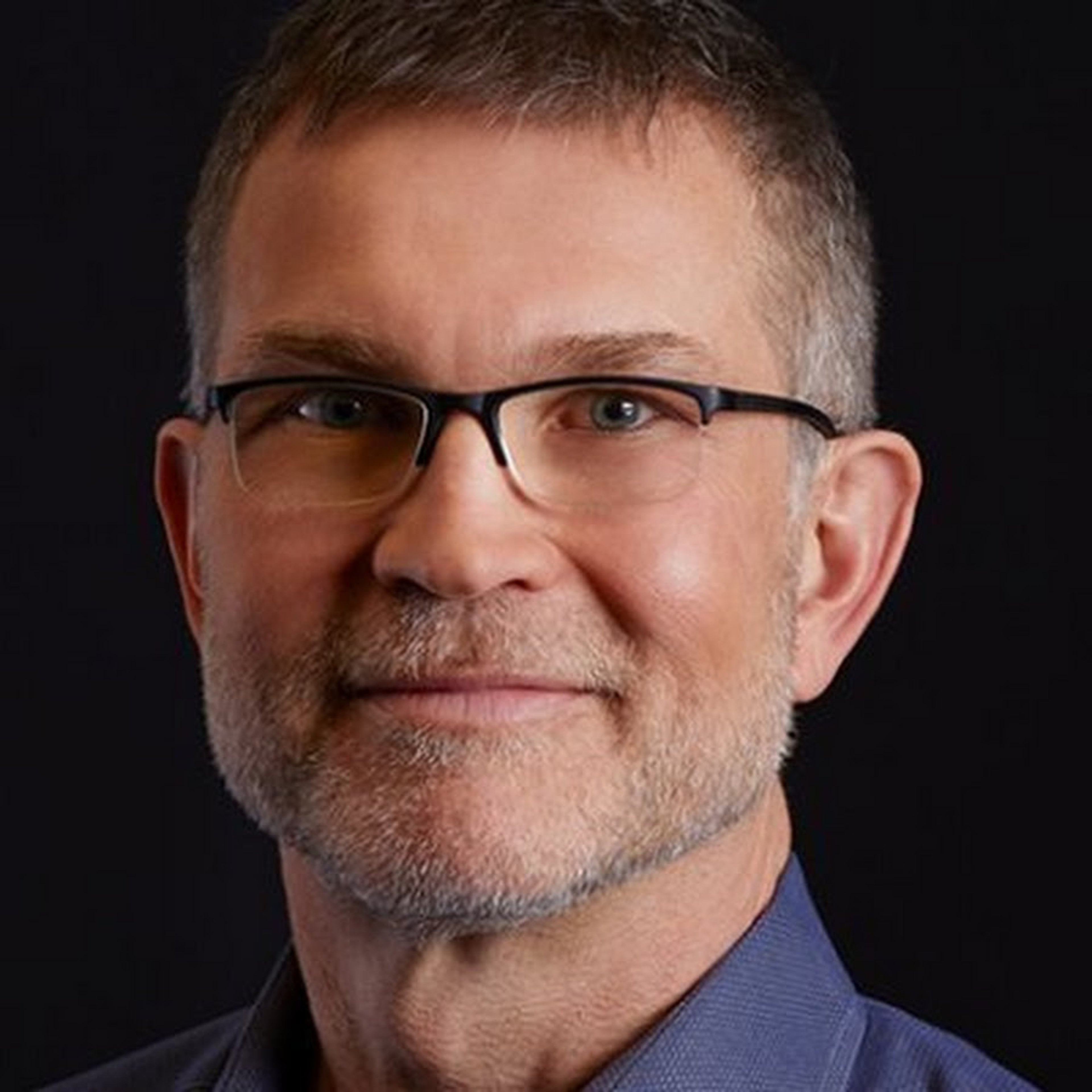 A middle-aged man with gray hair and a beard, wearing glasses and a blue collared shirt, with a friendly, professional demeanor.