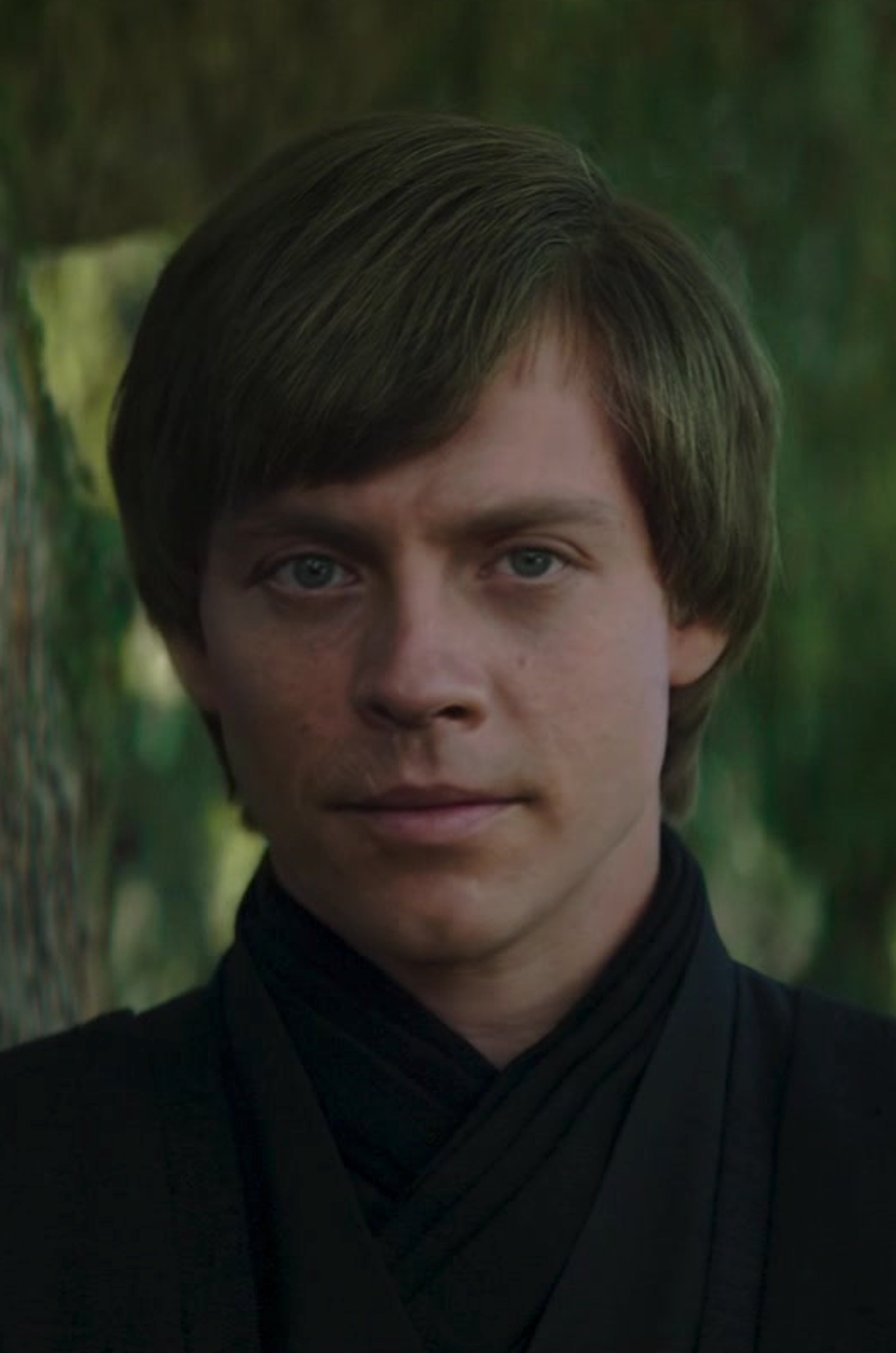A young man with sandy blonde hair, blue eyes, and a mechanical right hand wearing black Jedi robes