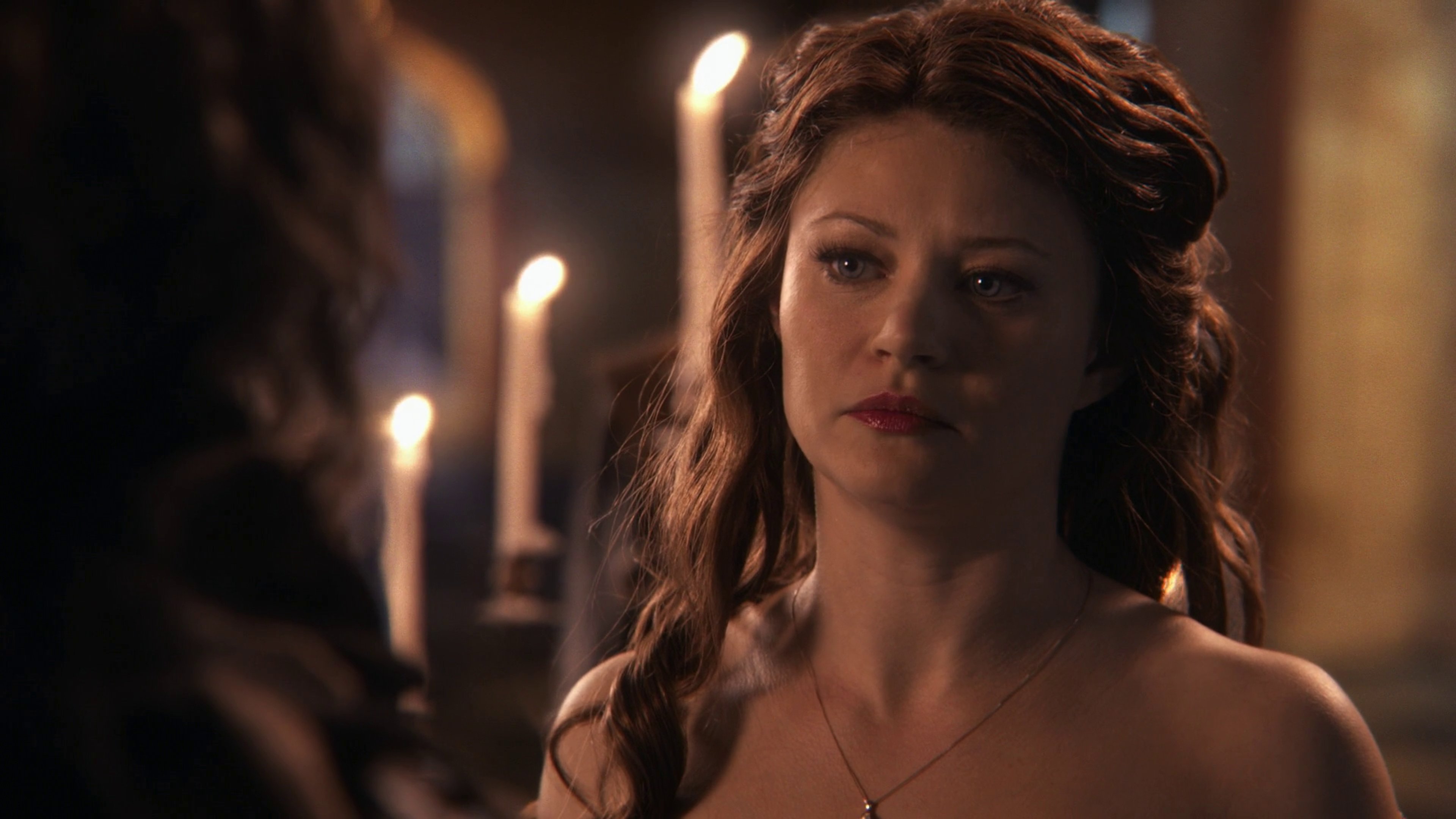 A woman with long brown hair wearing a blue and white dress, standing in a dimly lit room with candles.