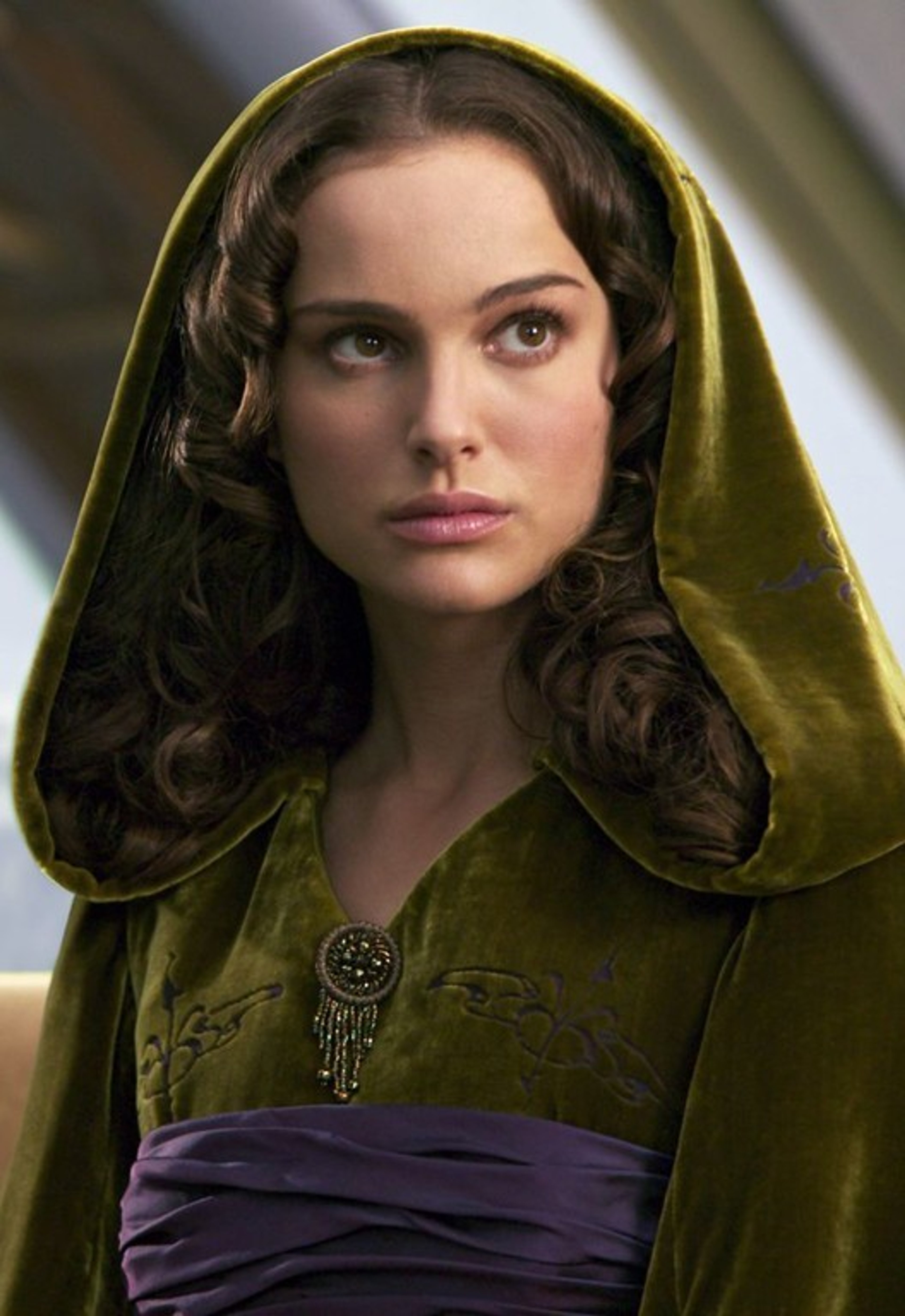 A woman with dark curly hair wearing a green hooded cloak