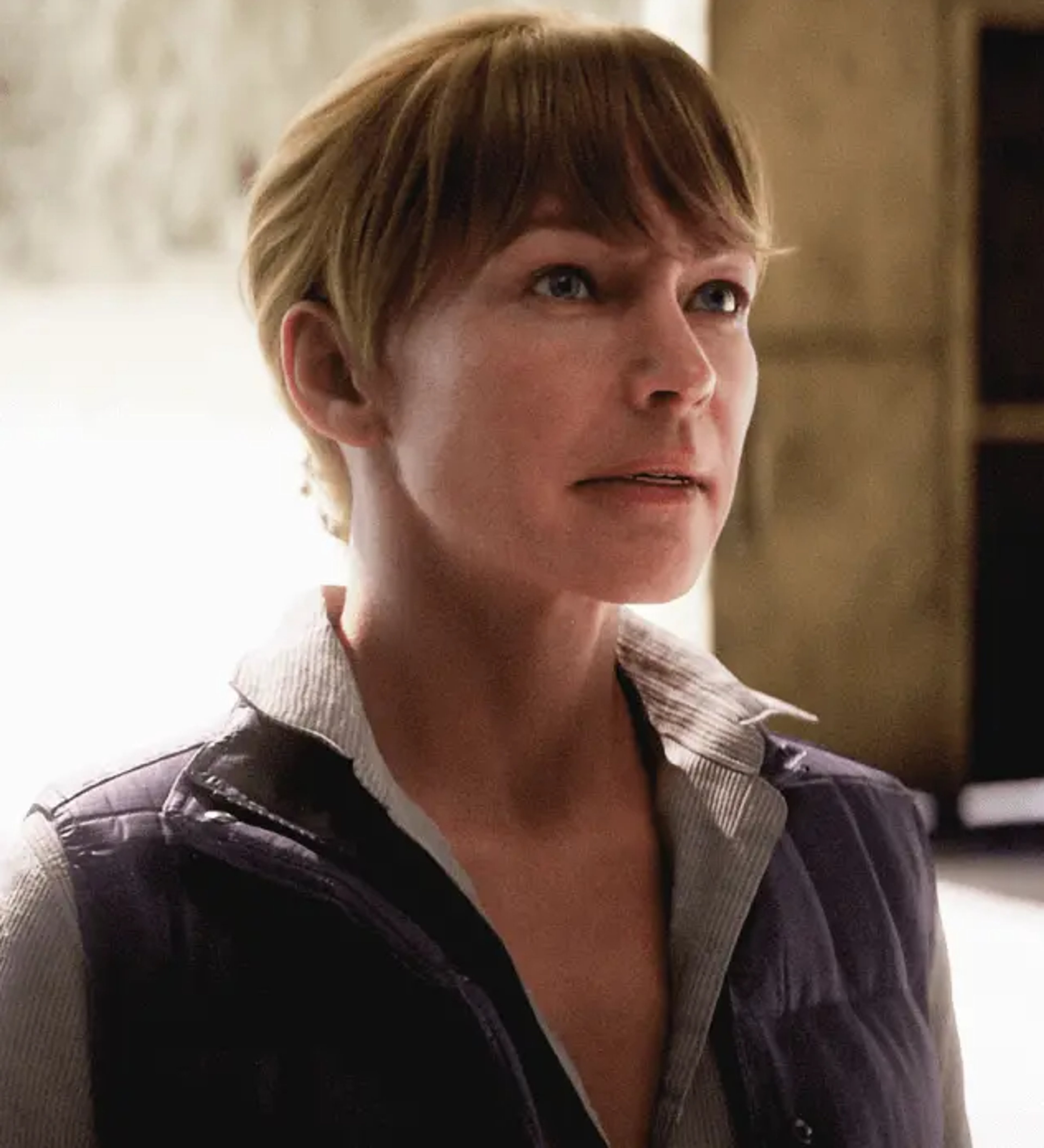 A middle-aged woman with short blonde hair wearing a black jacket, looking serious and focused.