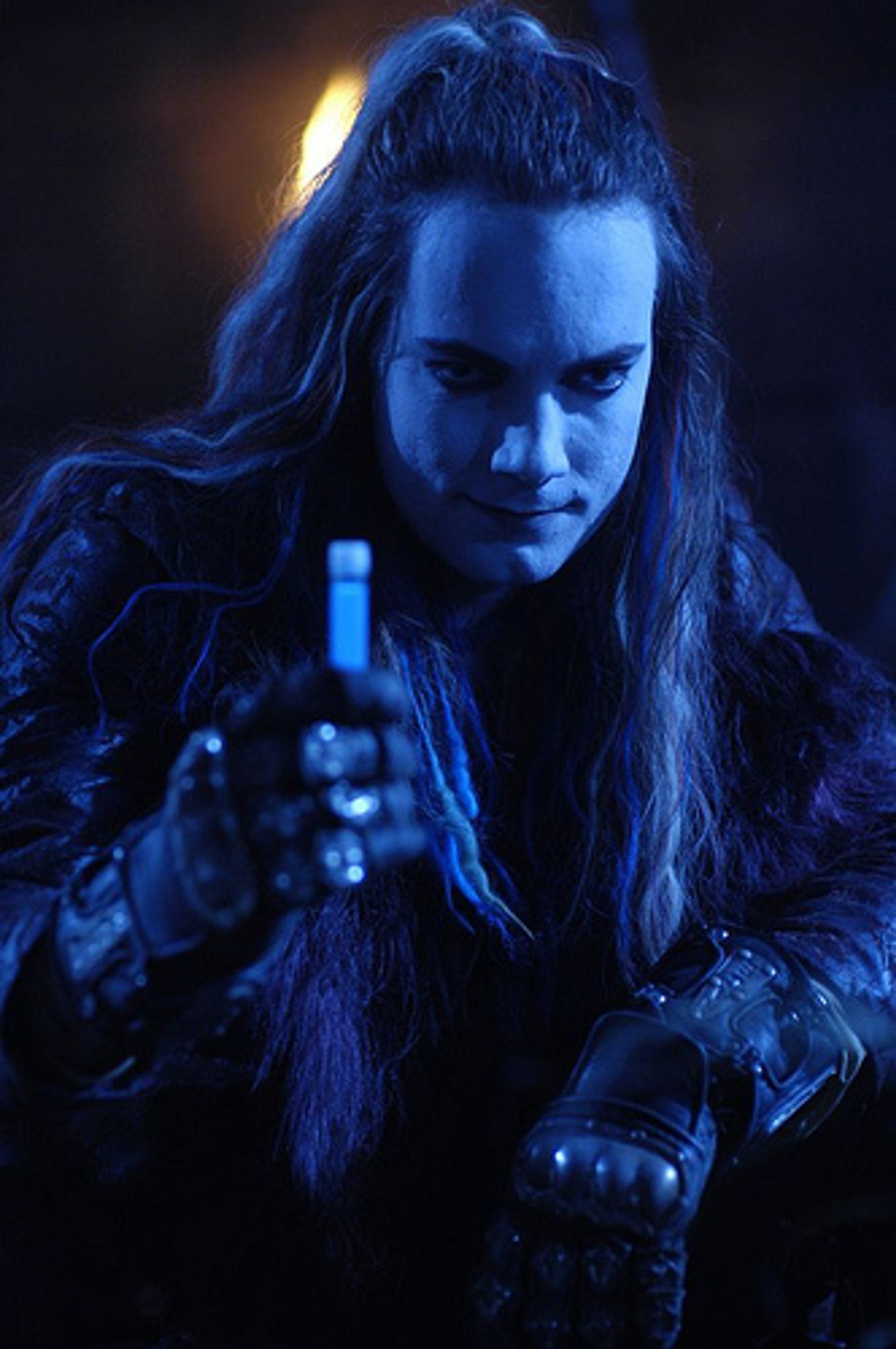 A dark, intense-looking person with long hair and a gothic-style outfit, holding an object in their hand.