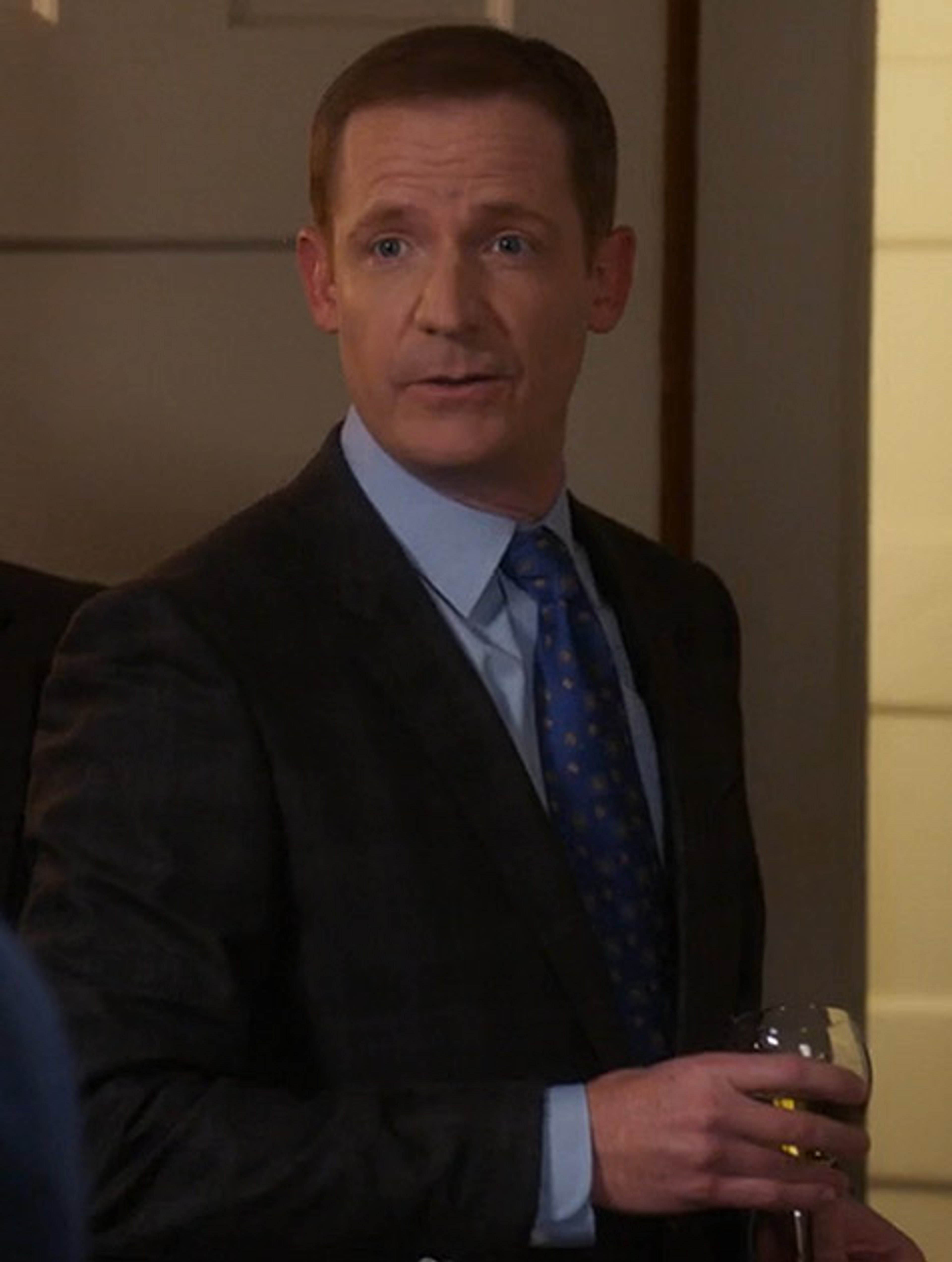 A middle-aged man in a suit and tie, with a serious expression